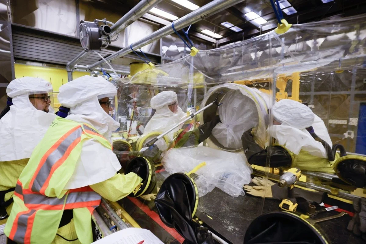 Newport News Nuclear BWXT Los Alamos waste processing operators repackage materials from a legacy waste container to a new lined drum in a mock-up glovebag exercise with nonradioactive materials. Glovebags are flexible plastic containers that allow 