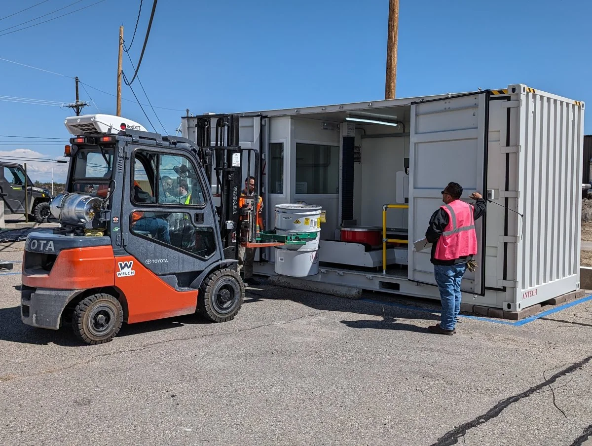  Workers place a container of legacy waste in the Universal Drum Assay and Segregation System at Technical Area 54 at Los Alamos National Laboratory, where the system is being demonstrated to more accurately analyze the radioactive contents in drums,