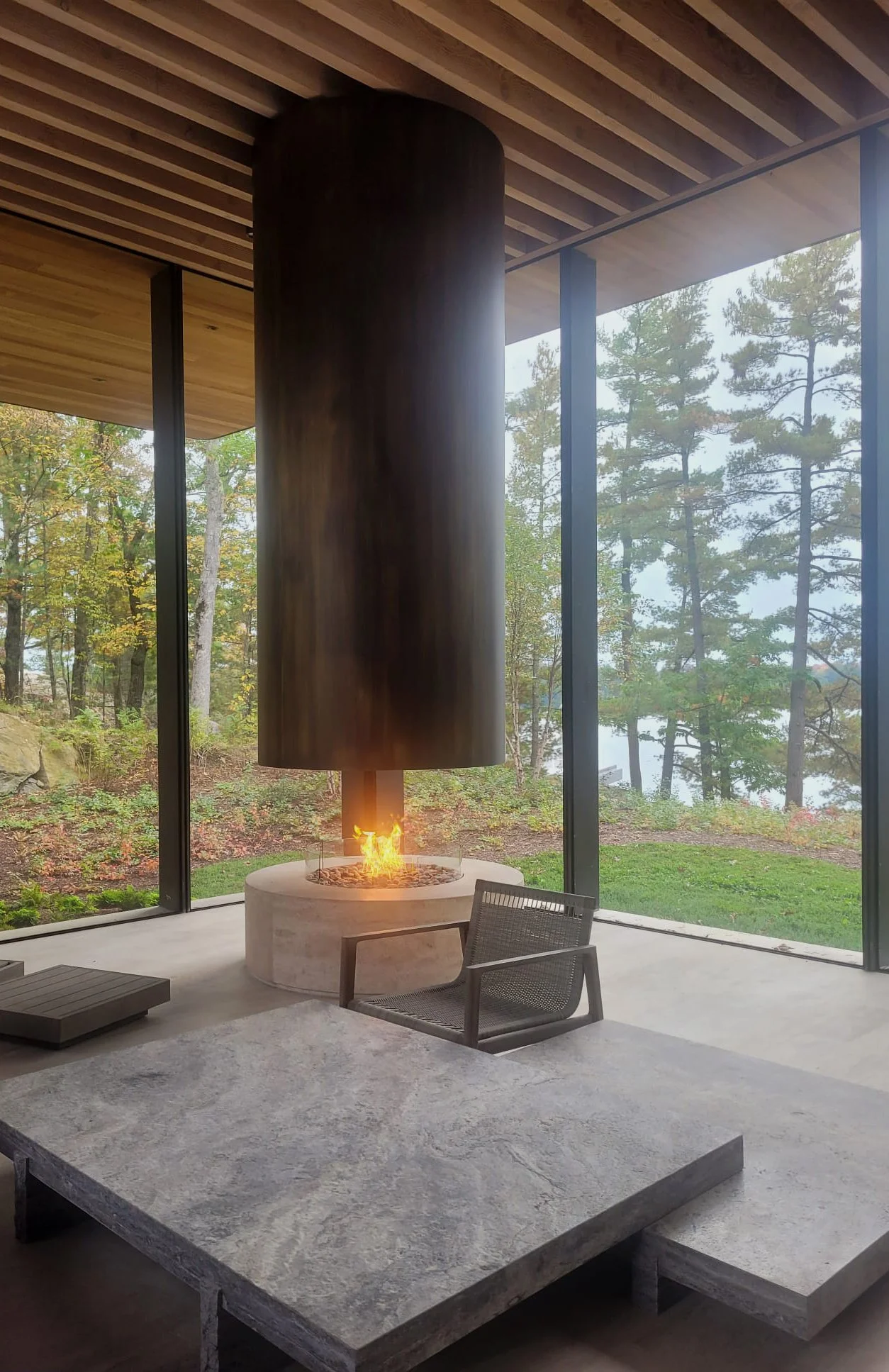 360-degree open concept Bordelet gas fireplace with bronze hood and concrete base in modern Muskoka cottage