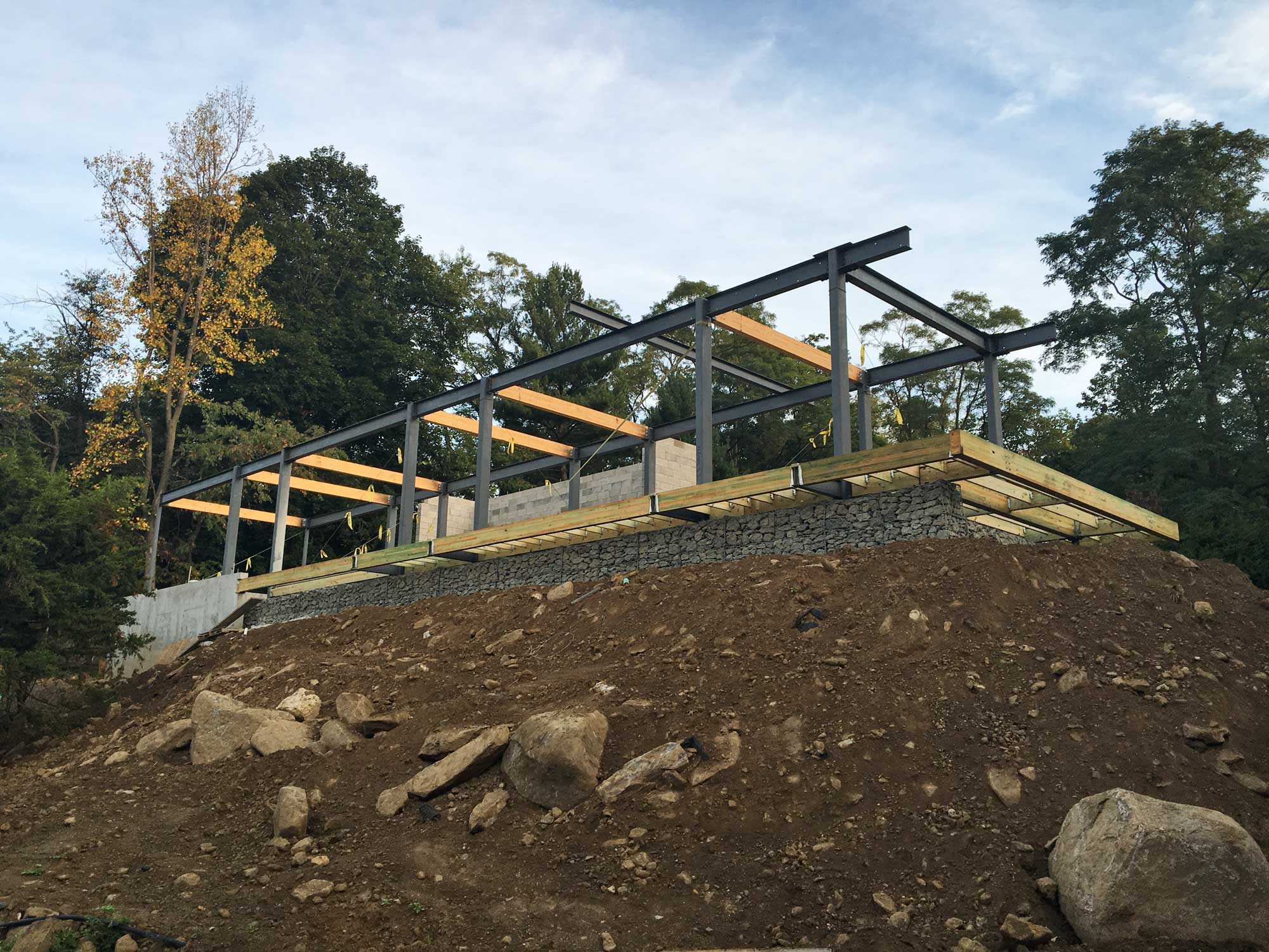 Steel Frame & Pool Deck -- A steel and wood pool deck cantilevers over a gabion retaining wall. The steel columns and beams are getting ready for the "bar" house to be framed above.