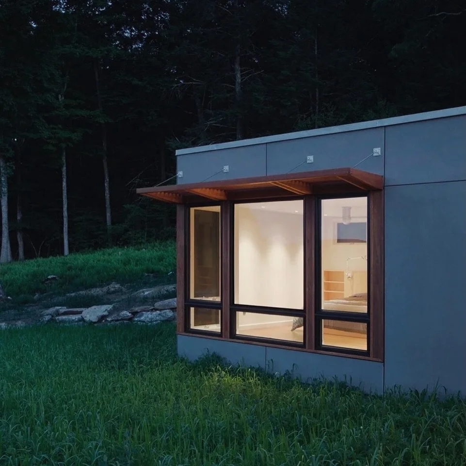A primary bedroom at dusk, framed by meadow and stone.

A rural site, defined by rocky outcroppings, sits at a high point with sweeping views of the Housatonic Valley.

Cement board panel siding establishes a low-maintenance exterior, while a natural