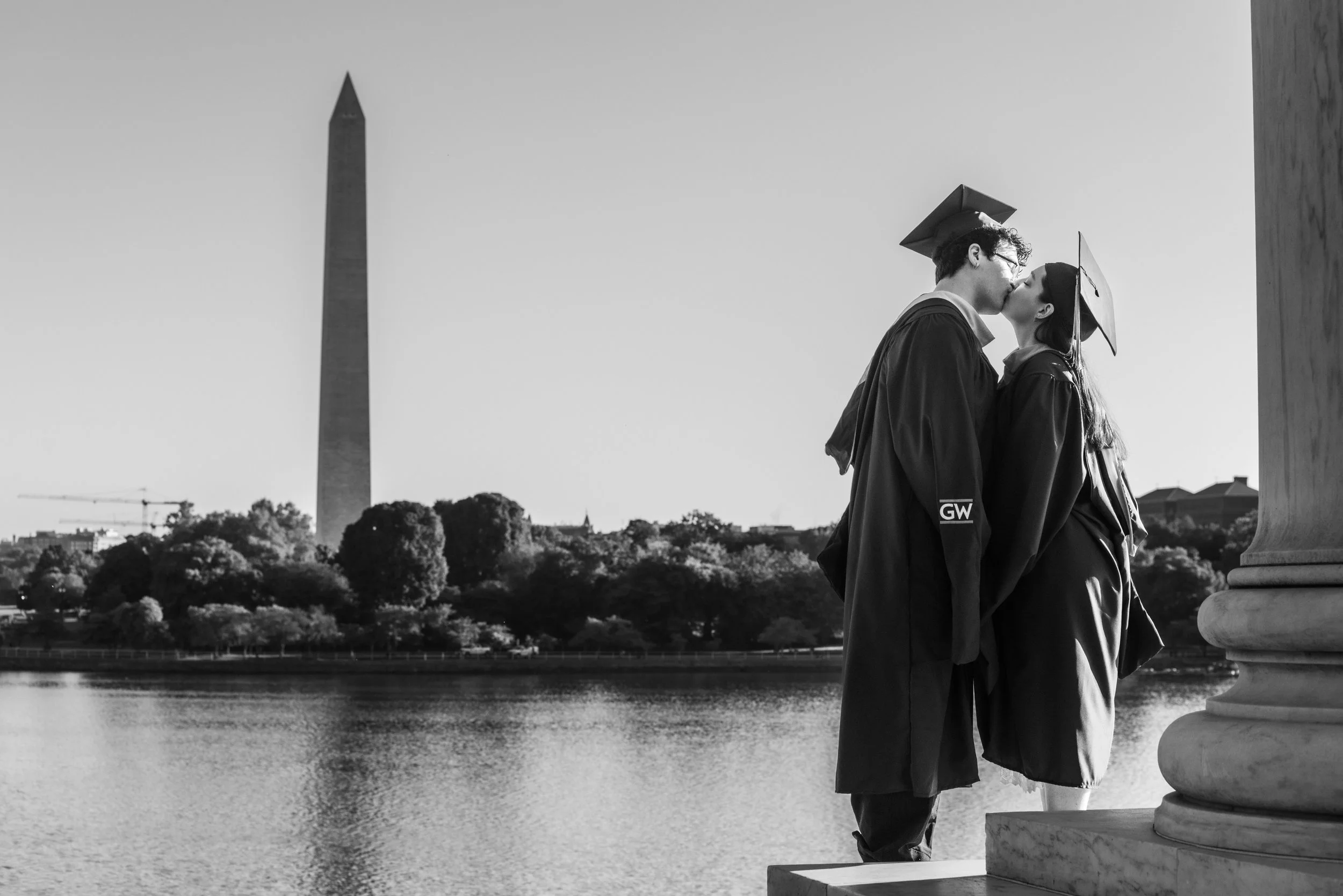 Two graduates sharing a kiss while standing on a ledge near the Washington Monument and the National Mall in Washington, D.C.