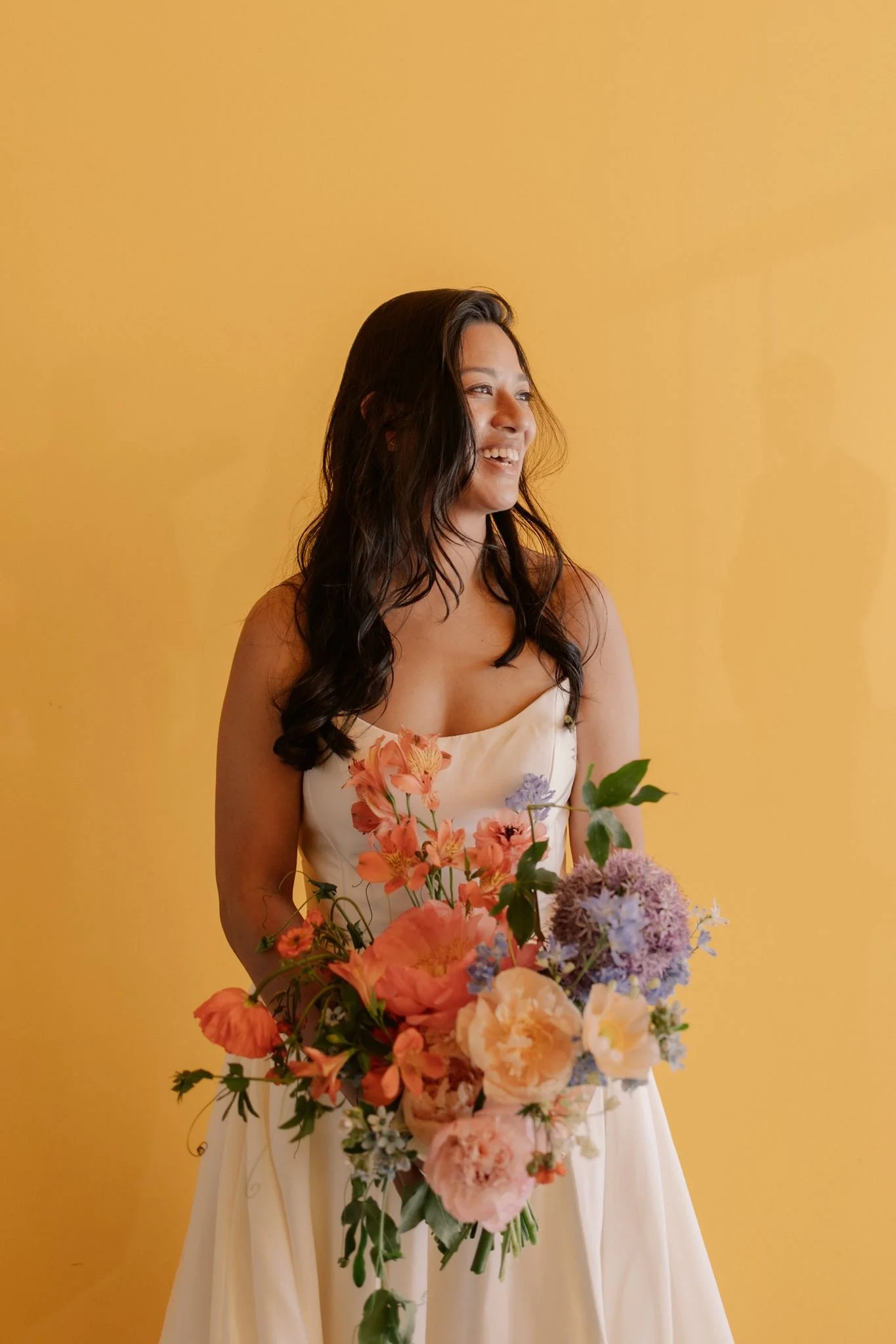 Bride holding peony and allium bouquet in front of yellow wall at Walker Art Center