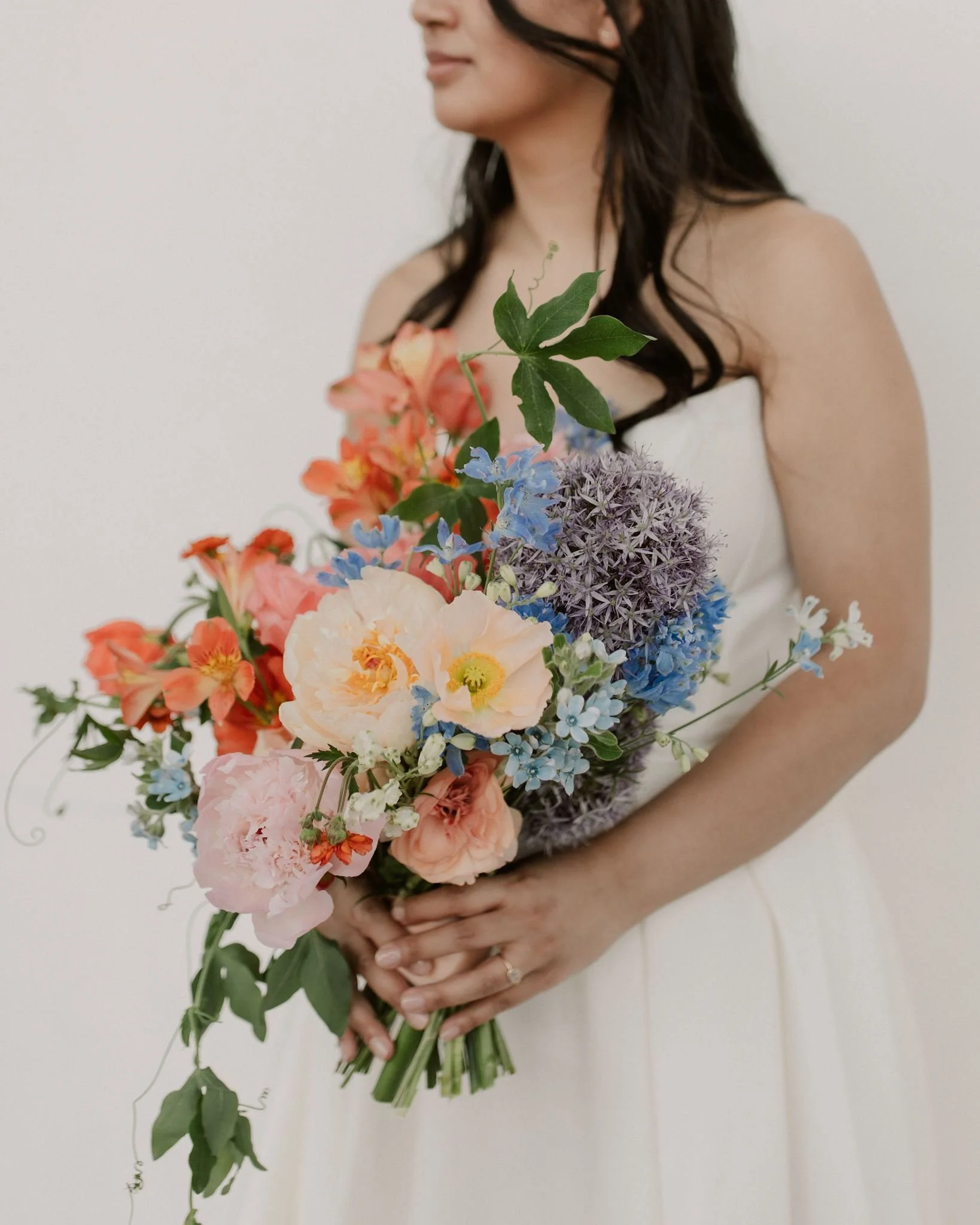 bride with oversized bouquet with peonies and allium, orange and pink with blue and purple