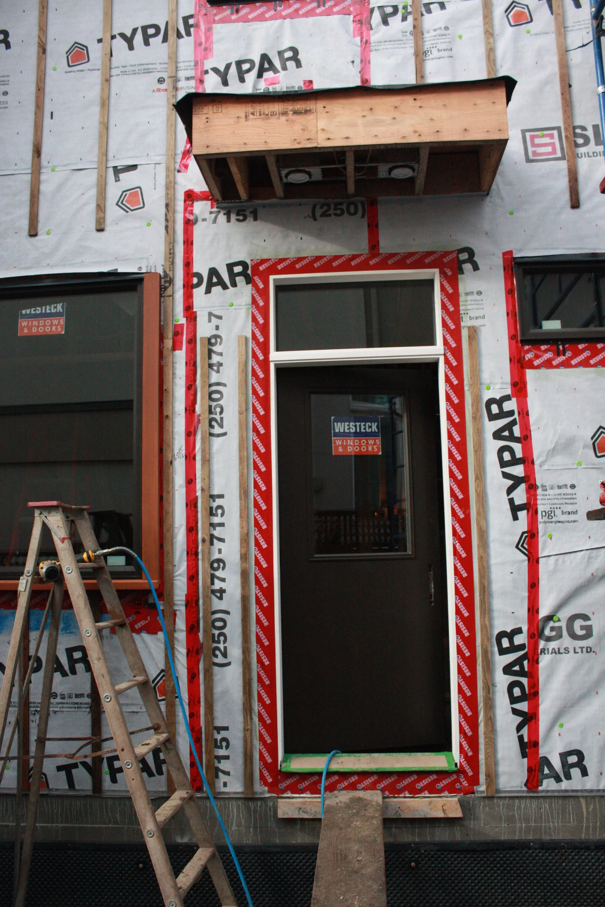 The back (East) door that demonstrates the window casing and trim along with the matching door colour. Can also see the exterior wall preparation for the siding and the foundation seal. 