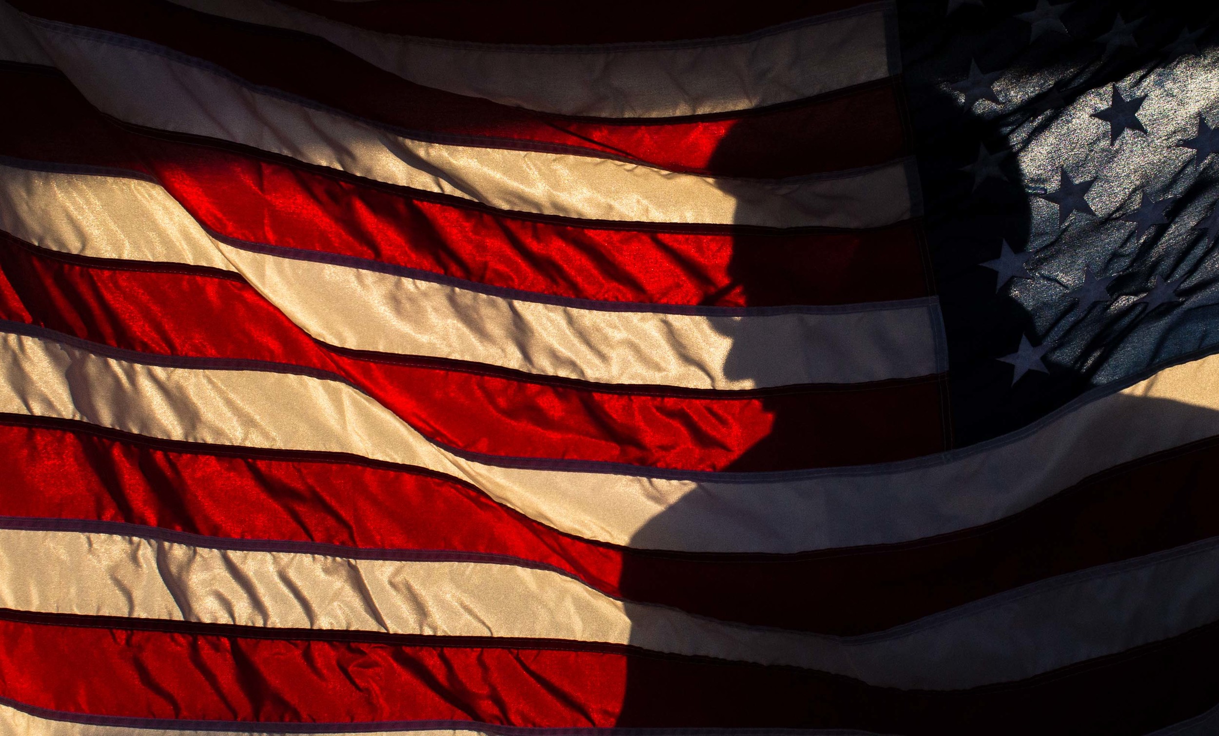 A man, silhouetted against an American flag, hands out tickets to people to see Republican presidential candidate Donald Trump speak at a campaign rally, Monday, Nov. 30, 2015 at the Macon Centreplex in Macon, Ga. (AP Photo/Branden Camp)