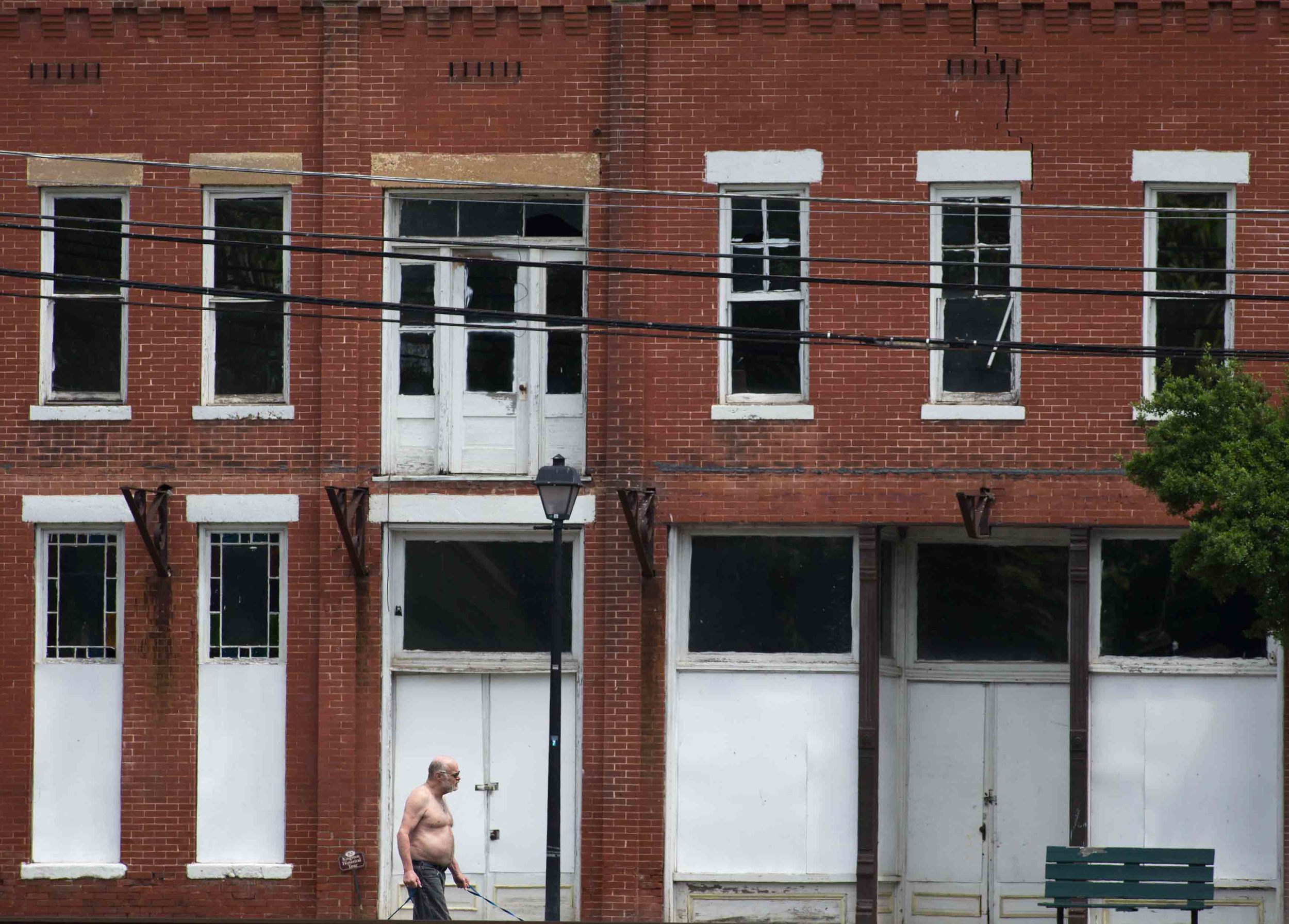 A Kingston resident walks his dogs past DeSoto Hotel, one of many vacant buildings in downtown Kingston. Photo by Branden Camp