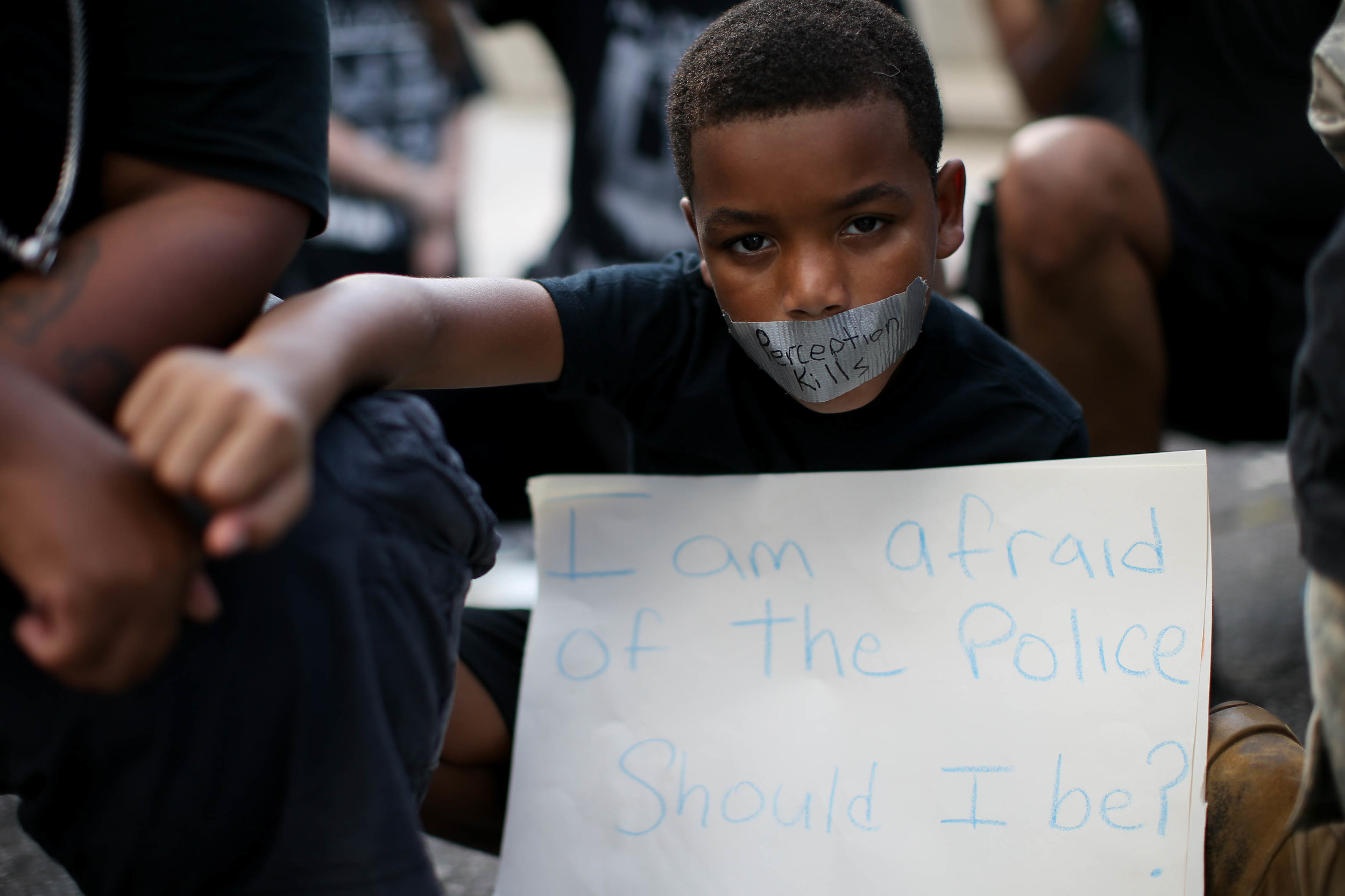 A young boy holds his fist up while wearing tape over his mouth during a Black Lives Matter protest at an entrance to Lenox Square Mall in Atlanta, Saturday, Sept. 24, 2016, in response to the police shooting deaths of Terence Crutcher in Tulsa, Okla. and Keith Lamont Scott in Charlotte, N.C. The Black Lives Matter chapter of Atlanta is boycotting major retailers following the recent police shooting deaths involving black men. (AP Photo/Branden Camp)