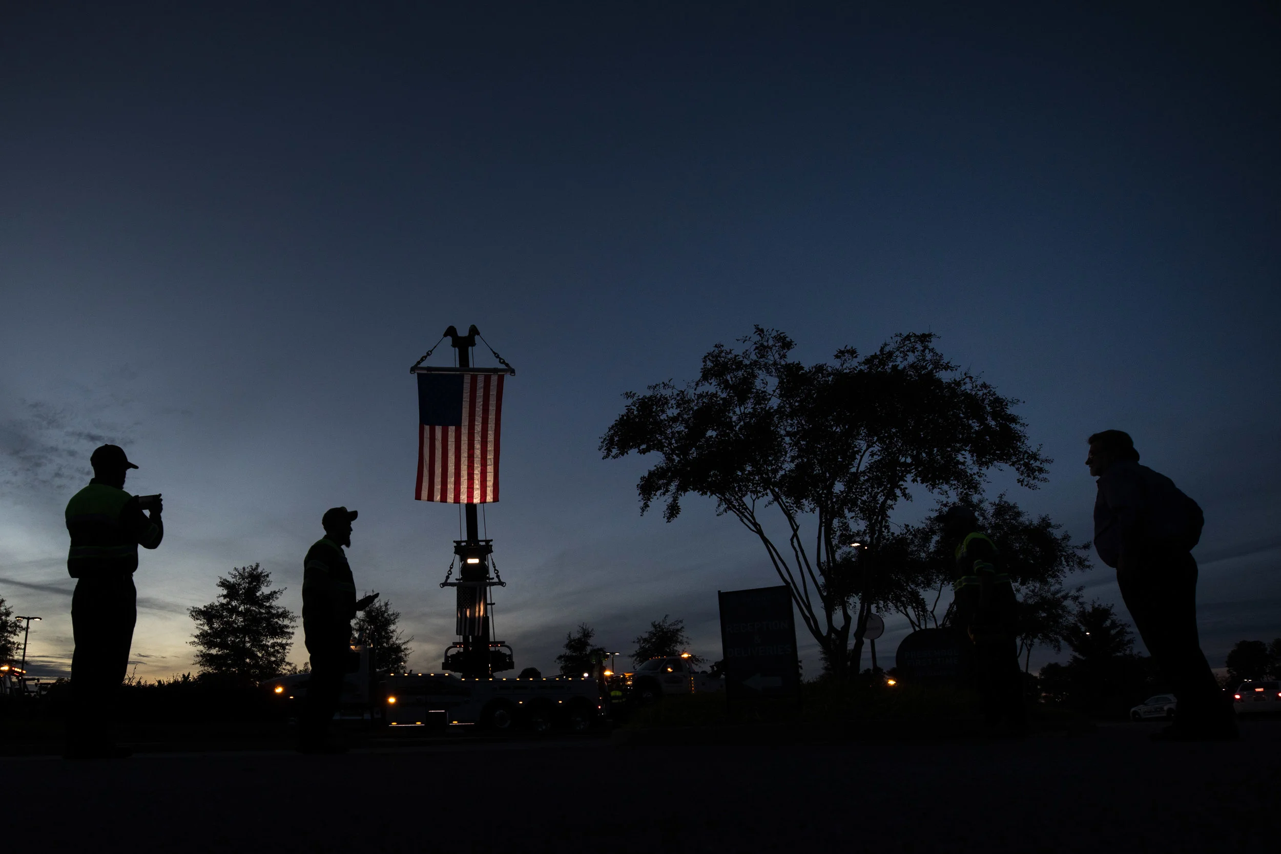 Statewide employees watch as an American flag and a Thin Blue Line flag hang from one of their tow trucks, a company that regularly worked with Gwinnett police officer Antwan Toney, who was killed in the line of duty, Monday, Oct. 22, 2018, in Sugar Hill Ga. A Gwinnett County police officer on Monday shot and killed Maynard, 18, accused of fatally shooting police officer Antwan Toney on Saturday near a school in the Atlanta area, police said. (Branden Camp/Atlanta Journal-Constitution via AP)