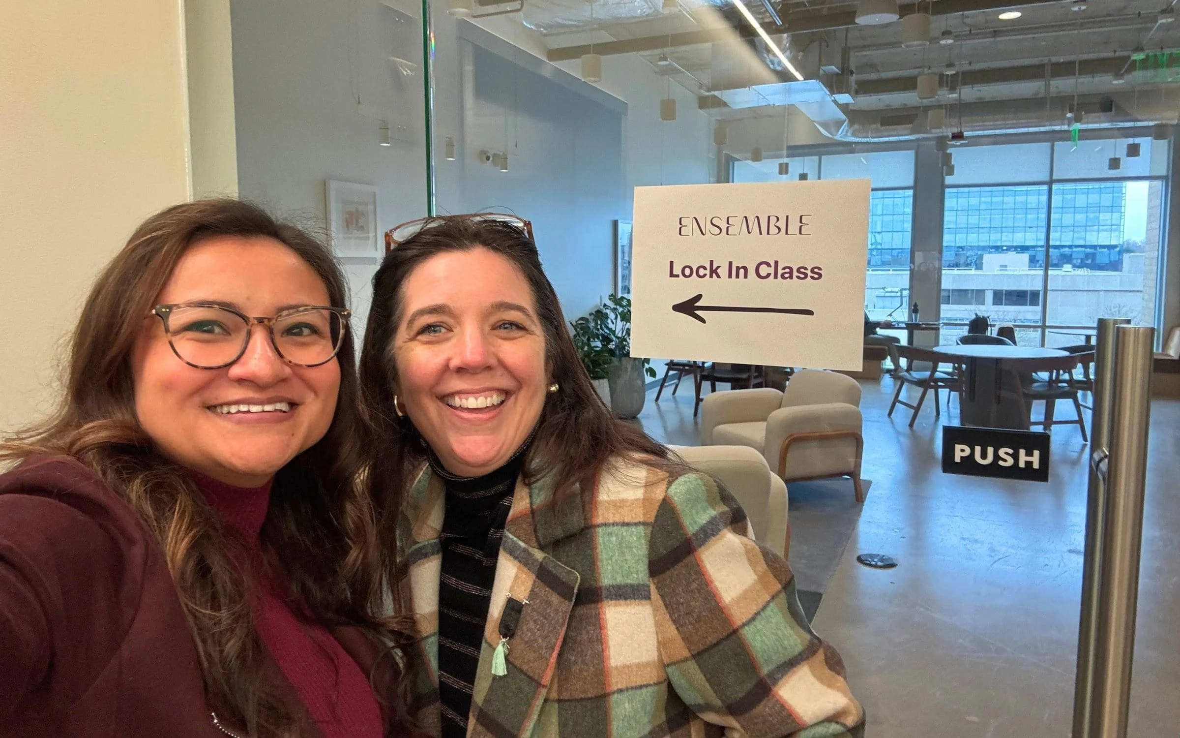 Alyssa Christensen and Marguerite Martin smiling at Ensemble in Seattle beside a sign directing attendees to their Lock In class.