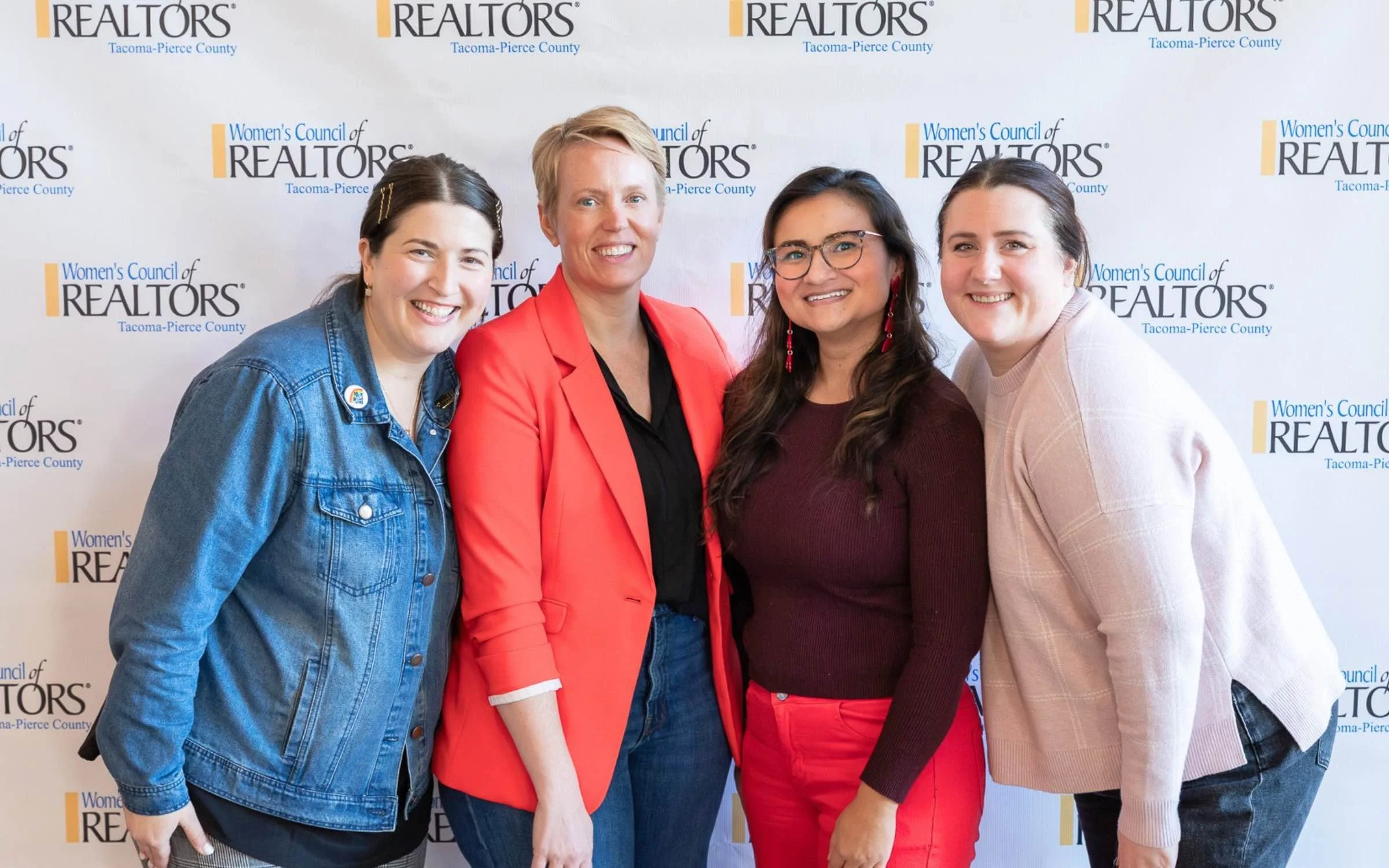 Four women smiling together in front of the Women's Council of REALTORS Tacoma-Pierce County event backdrop