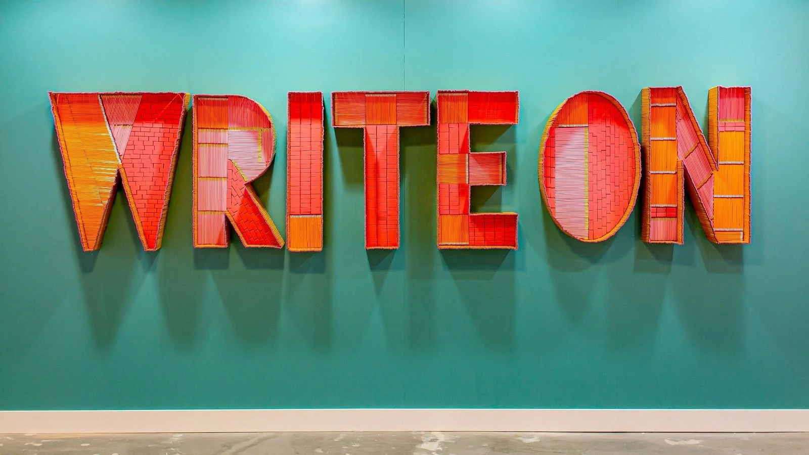 Colorful red and orange letters spelling “WRITE ON” against a teal wall, representing creative writing and storytelling. Photo by Jake Nackos on Unsplash.