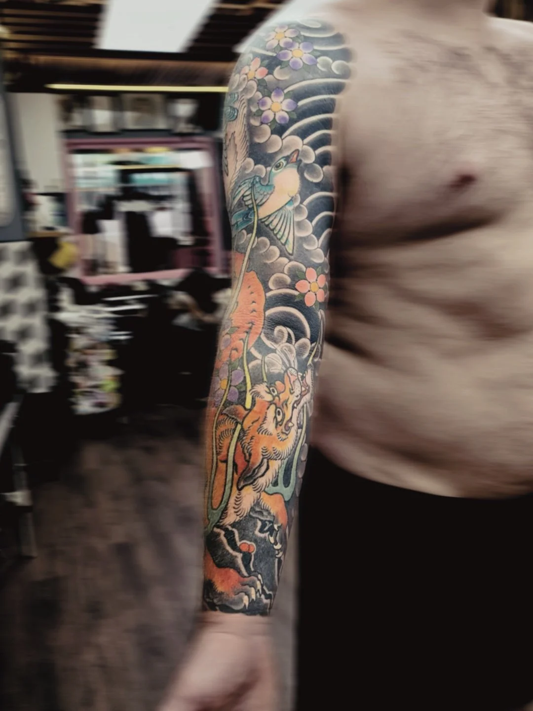 Tattoo sleeve featuring a colorful bird, a fox, and floral elements on a man's arm.