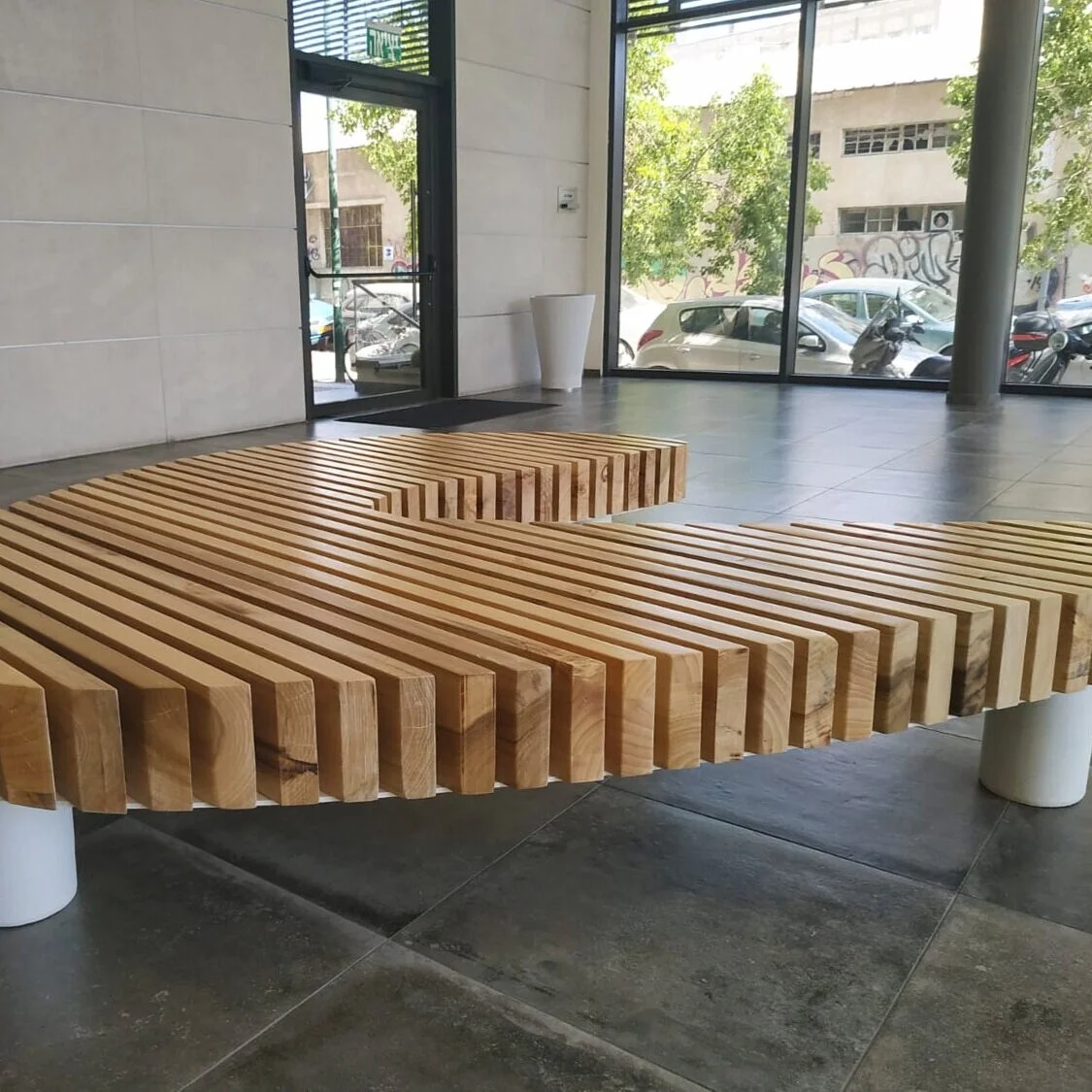 ספסל עץ גדול בצורת C עם רגלי מתכת לבנות בלובי בניין, מבט מלפנים
