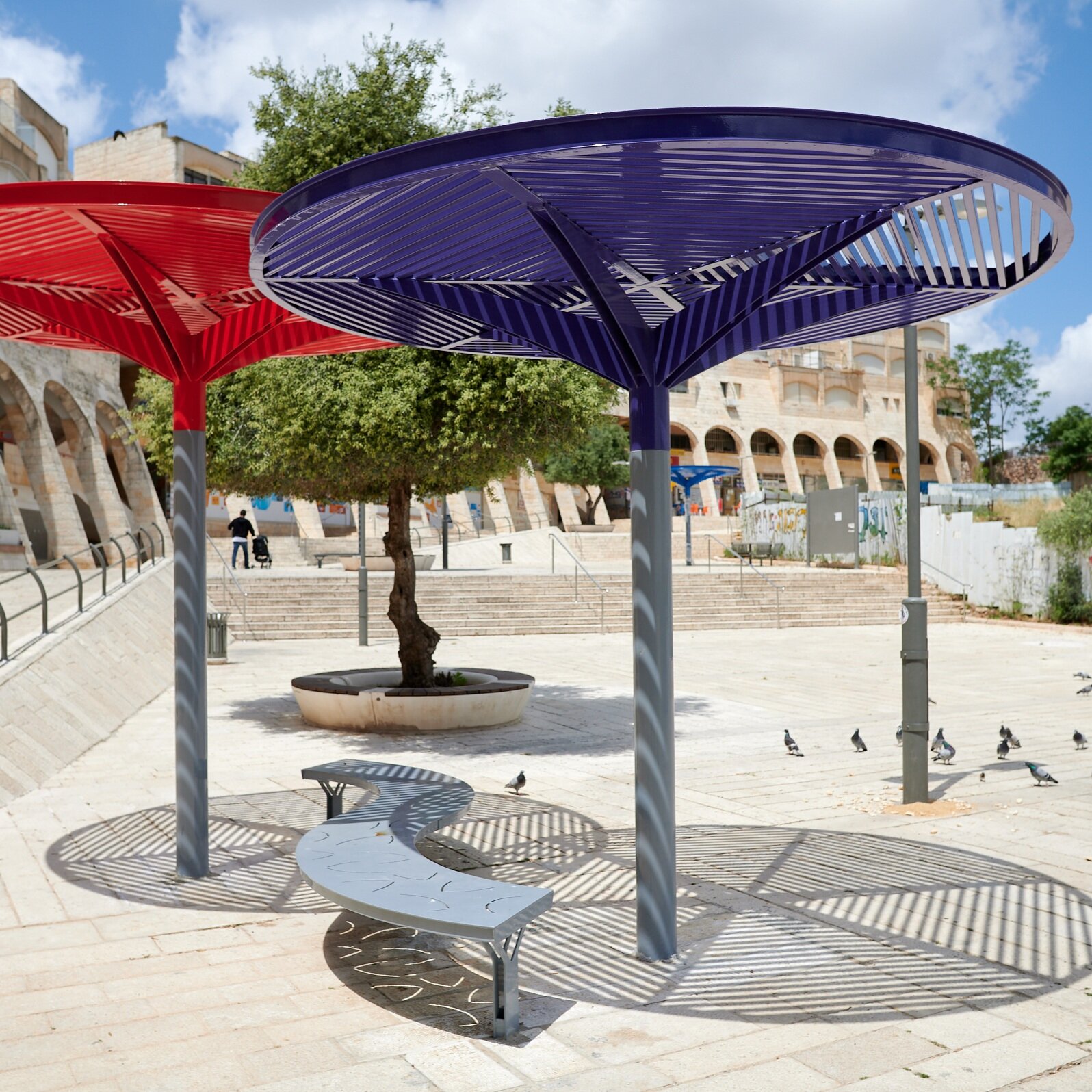 פביליון הצללה אדום וסגול ממתכת צבועה עם ספסל S במרכז מסחרי בגילה
