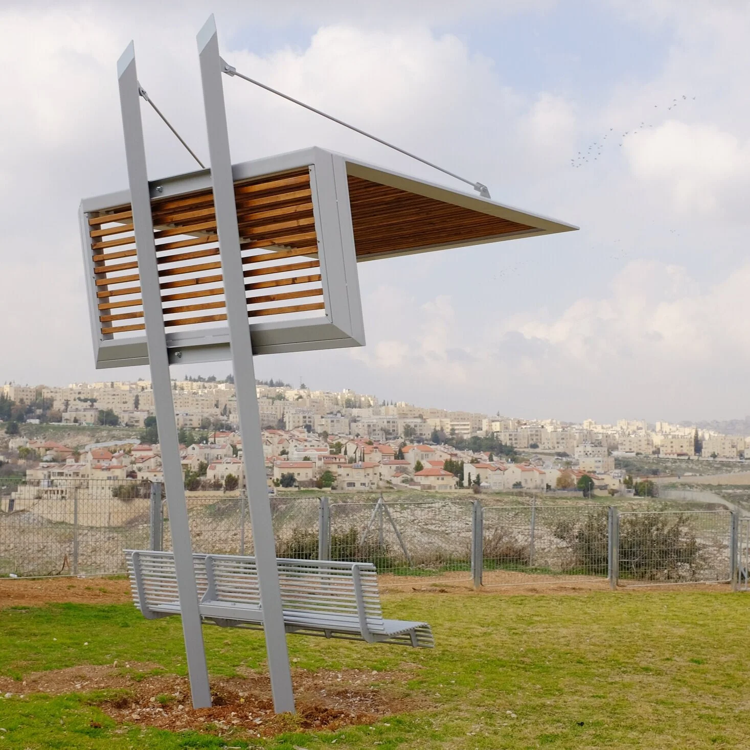 פביליון הצללה ממתכת ועץ עם גג מוטה ומתיחי כבל, ספסל מתכת משולב, נוף לירושלים ברקע