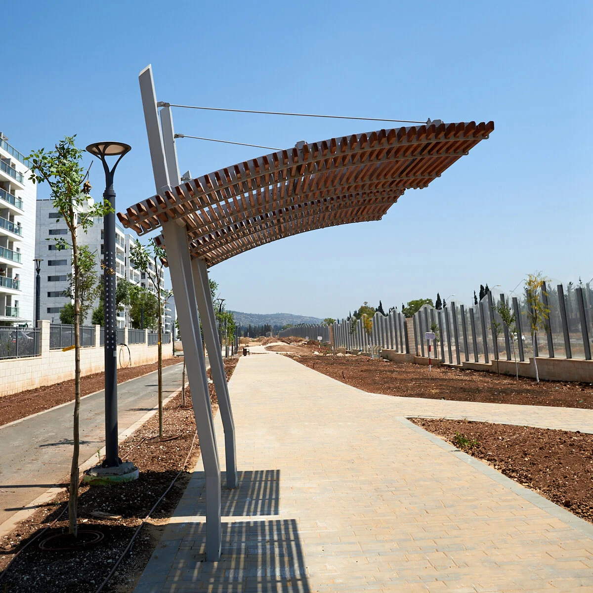 פרגולת ורטיגו בודדת ממתכת ועץ עם ספסלים מתחתיה, צילום מלמטה על רקע שמיים