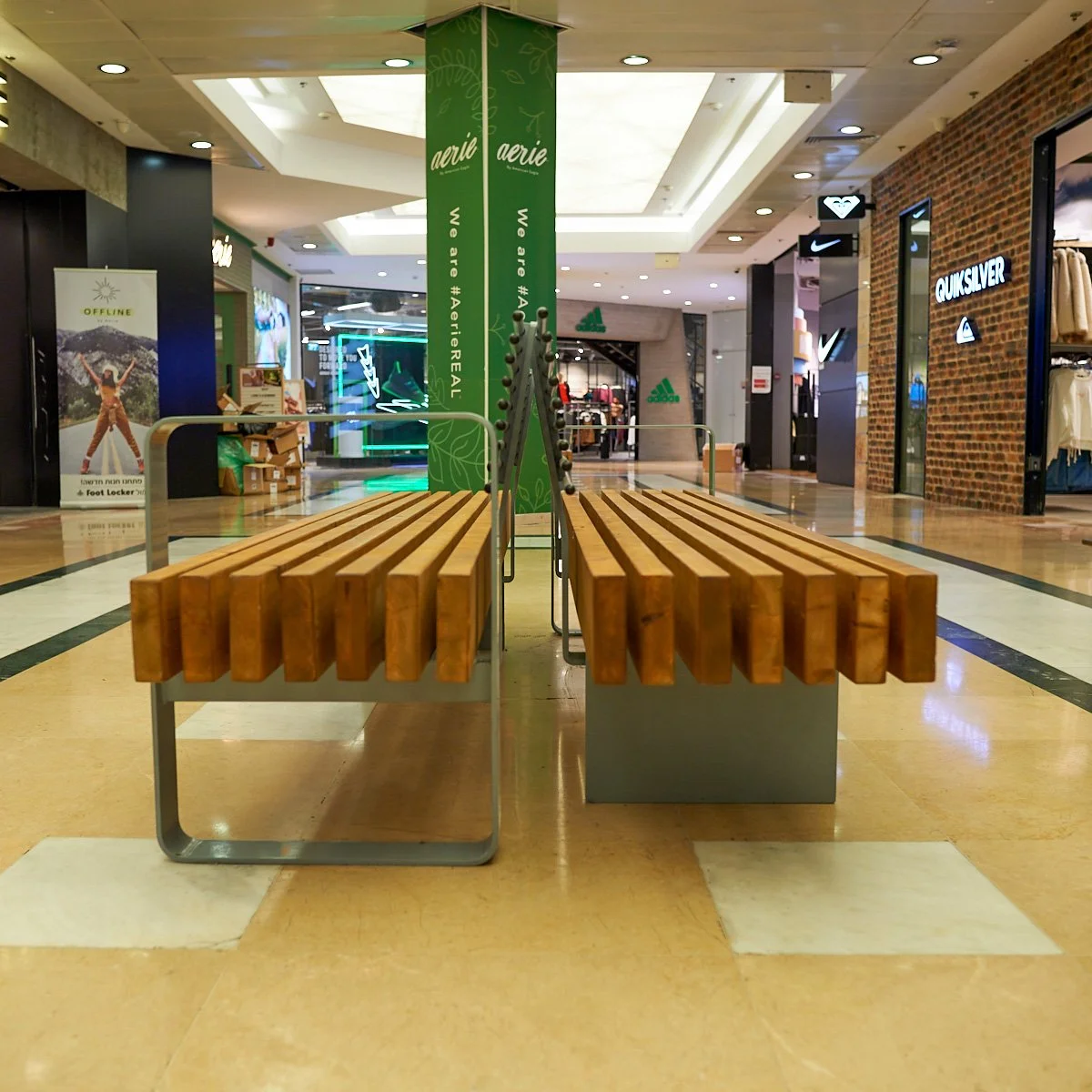 ספסל מעץ בצורת קשת עוטף עמוד עגול, בסיסי מתכת כתומים, אולם תצוגה עם תמונות טבע על הקיר