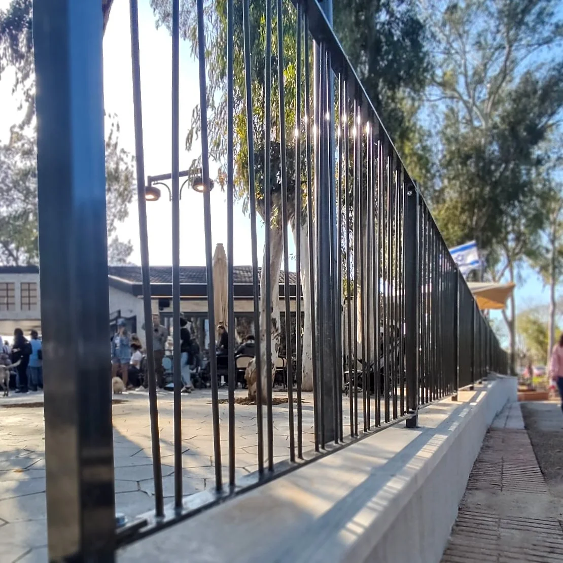 גידור מתכת לאורך שביל הולכי רגל בפארק, ילדים ומבוגרים חולפים משני עברי הגדר