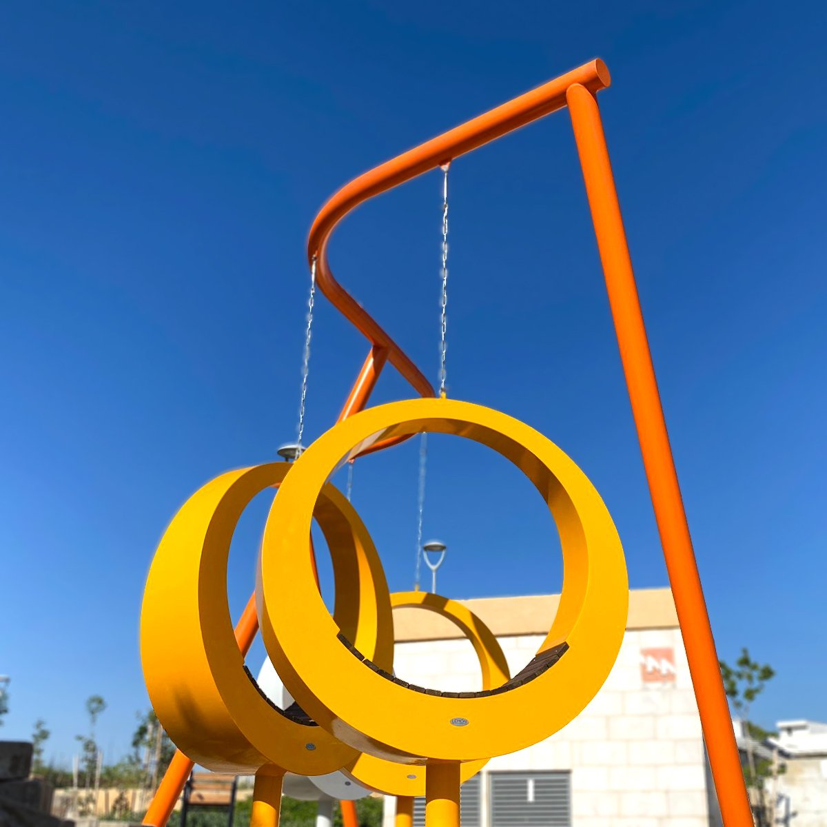 מבט רחב על מערכת Swivel – מסגרת מתכת כתומה עם שתי טבעות ישיבה צהובות ולבנות תלויות על רצפת אבן