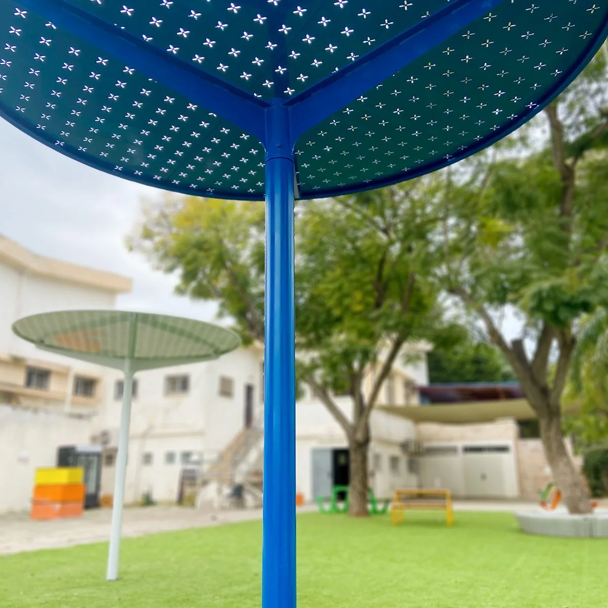 שולחנות עגולים ממתכת גלם עם מושבים משולבים על משטח כחול בחצר בית ספר