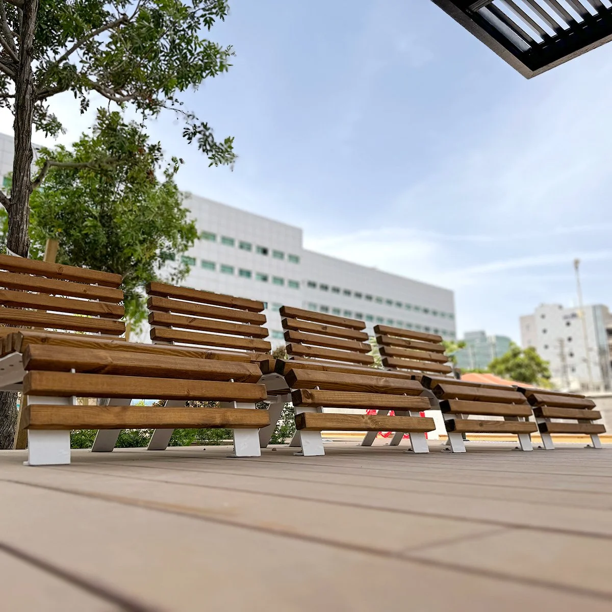 ספסל ארוך מעץ ומתכת לבנה מול חזית זכוכית של בניין מגדל סיבים