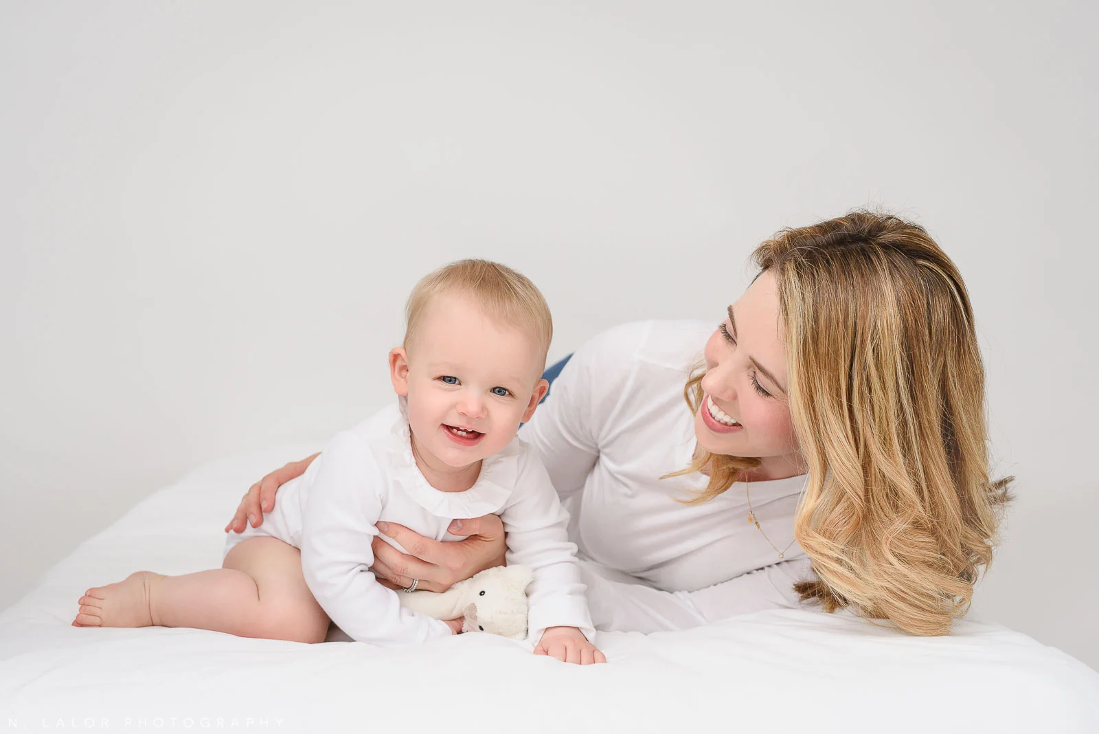 Image of a mother and her daughter, playing and laughing on a white bed. Studio portrait by N. Lalor Photography. Greenwich, Connecticut.