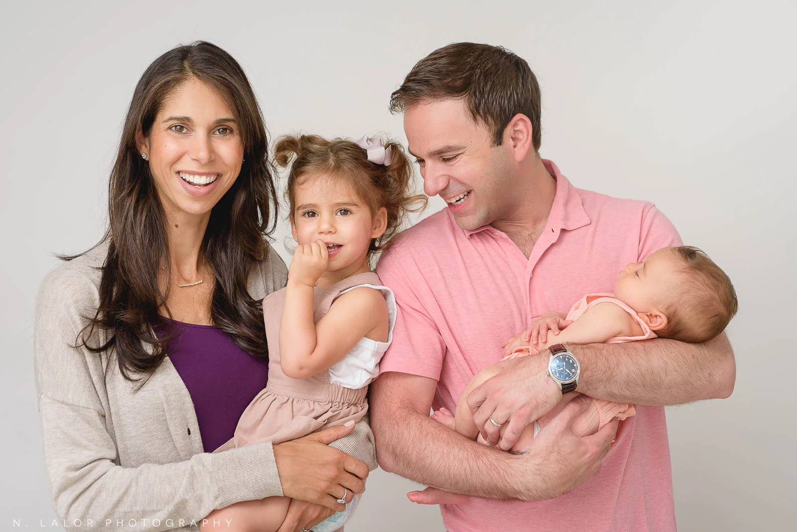 Image of a happy family with a toddler girl and new baby. Studio family portrait by N. Lalor Photography in Greenwich, CT.