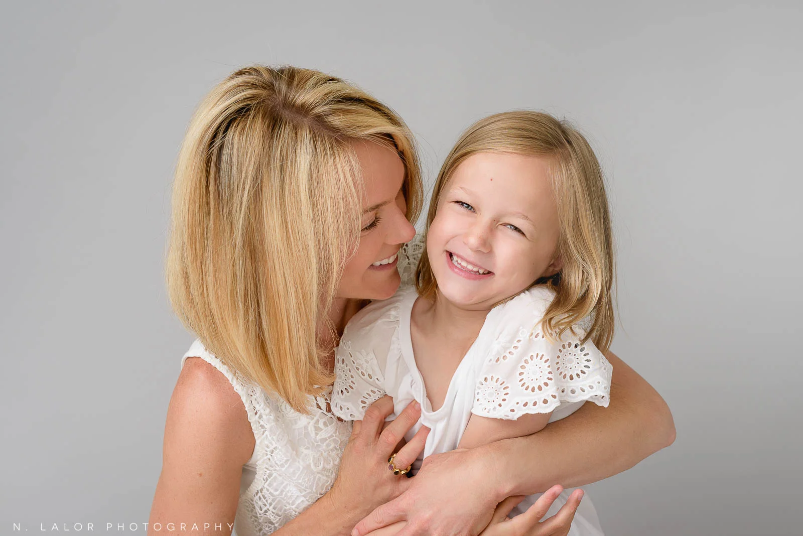 A spontaneous-looking photo between a mother and her daughter. The mother is hugging her daughter close while they both giggle in a shared moment of joy. Photo of N. Lalor Photography Studio in Greenwich, Connecticut.