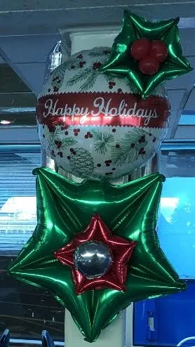 Decorative holiday balloons including a large round balloon with holiday graphics and a red "Happy Holidays" message, surrounded by green and red star-shaped balloons with metallic finishes.