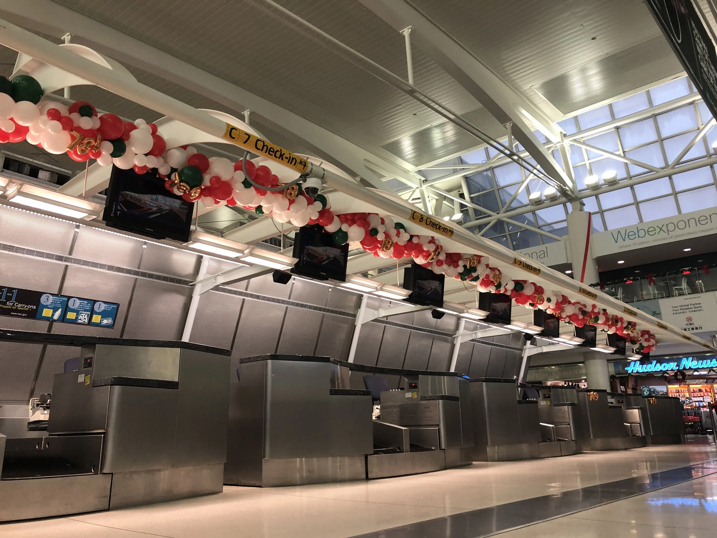 Empty check-in counters at an airport decorated for the holiday season with red, white, and green balloons.