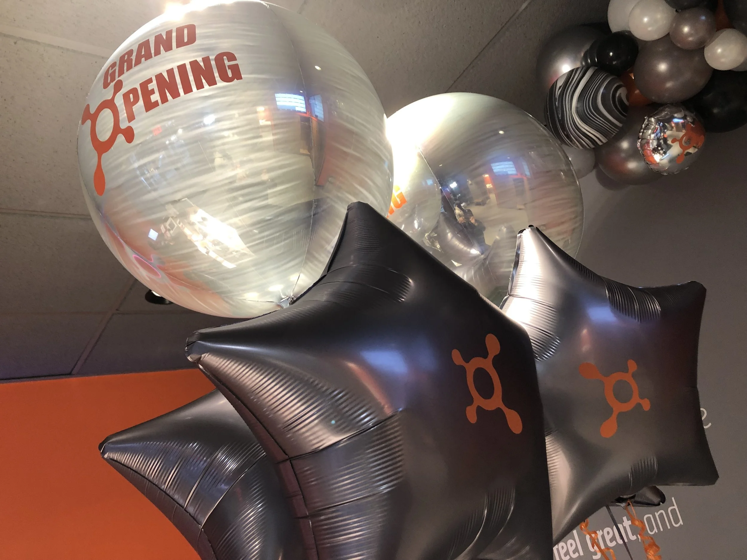 Silver and black balloons with orange logos and text, celebrating grand opening of an Orange Theory location.