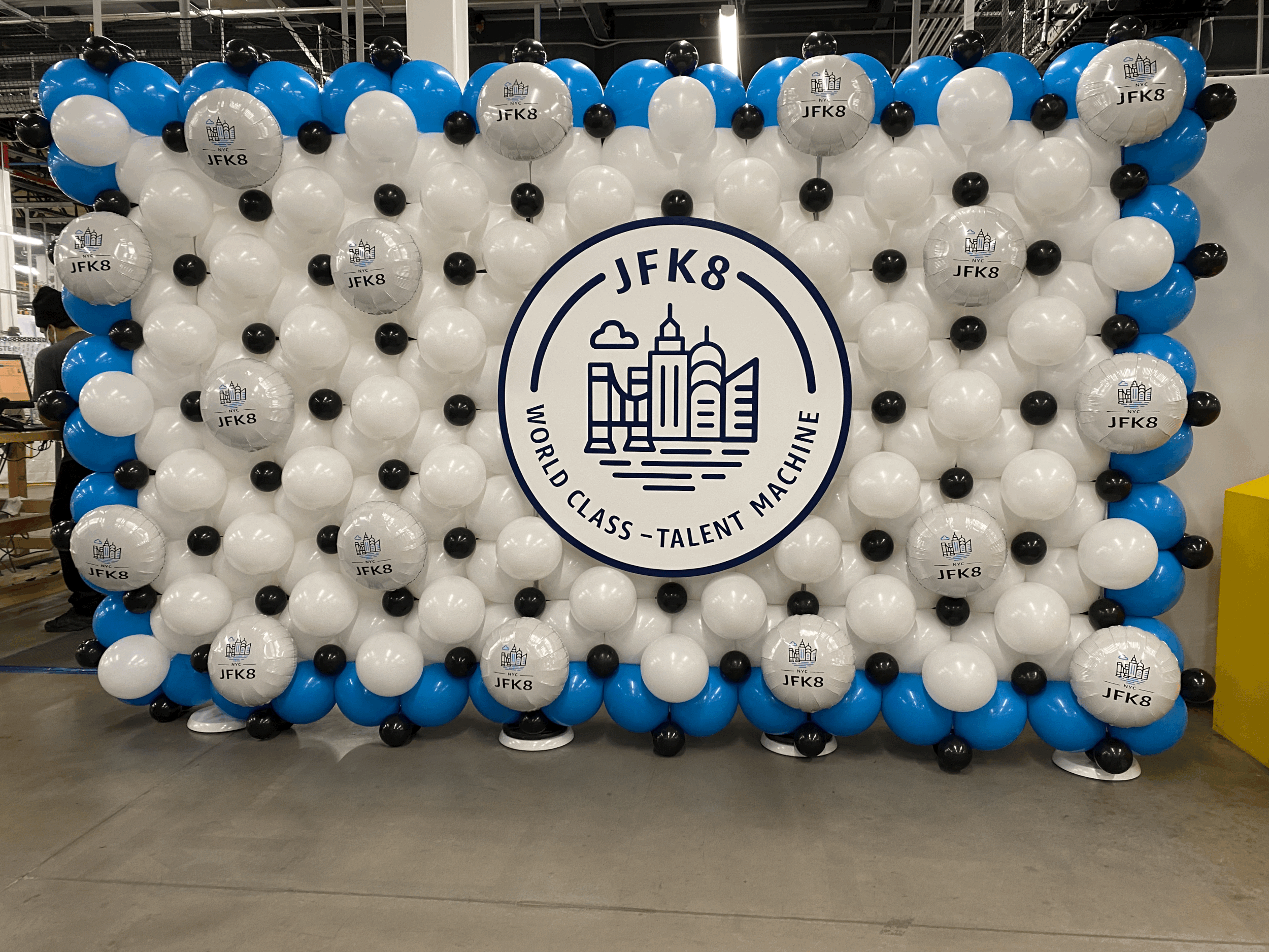 Balloon display with a Central logo reading 'JFK8 World Class Talent Machine' surrounded by white, black, and blue balloons in an industrial setting.