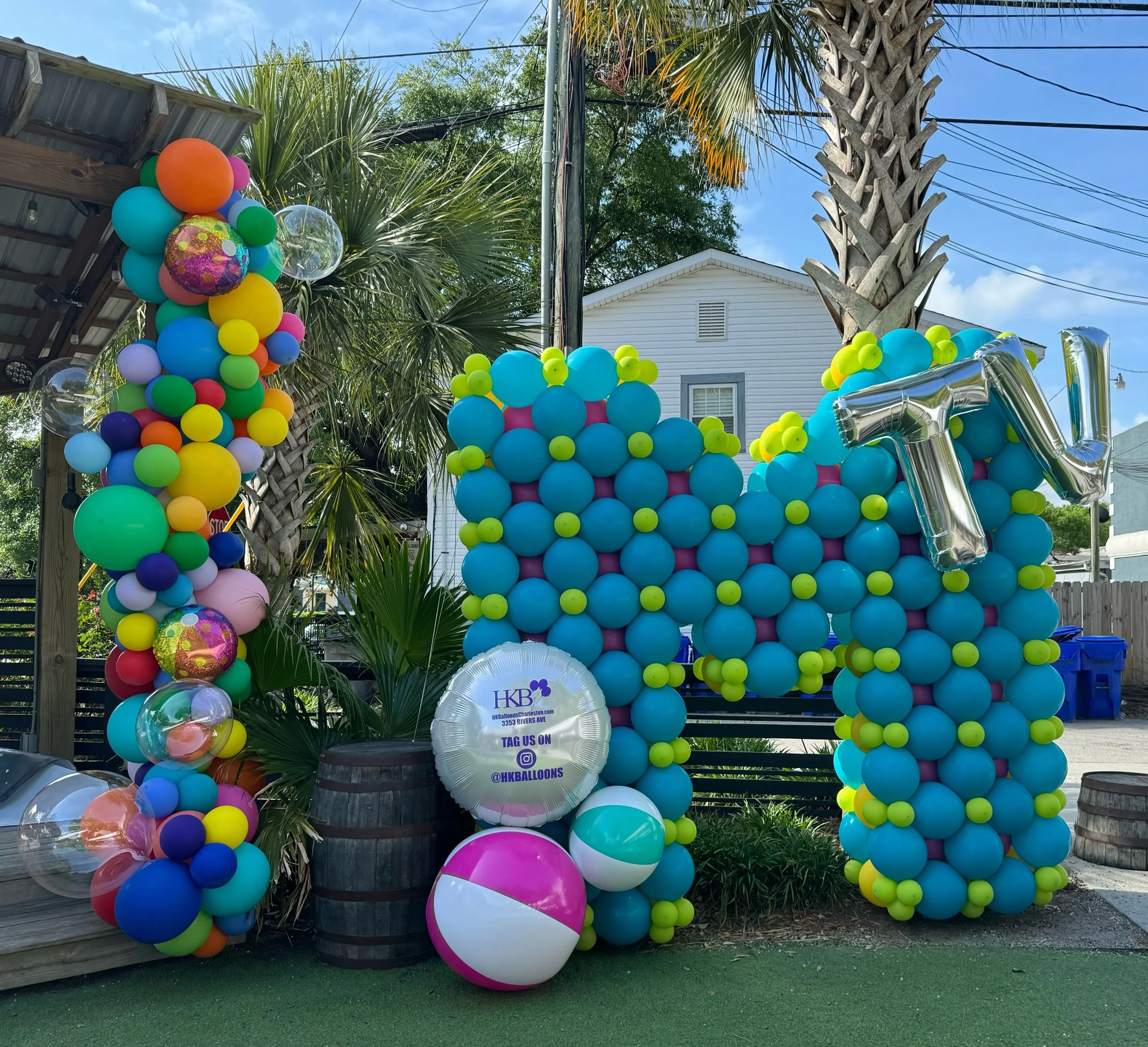 Custom balloon order that has blue balloons shaped into a giant M. There are beach balls with a vertical wreath of multi-color balloons.