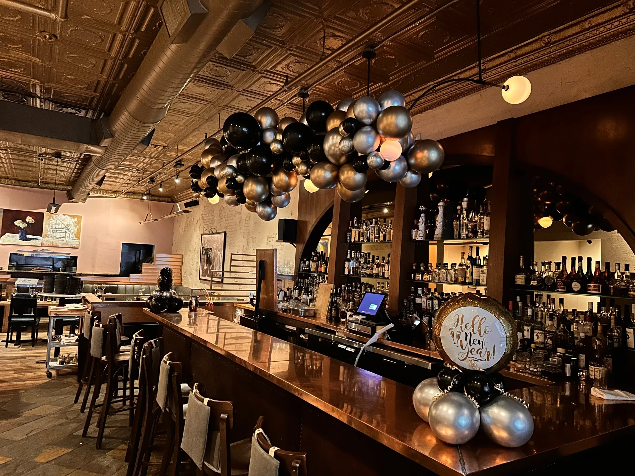 A bar decorated with black, silver, and gold balloons and a sign that says 'Hello New Year!' for a New Year's celebration.