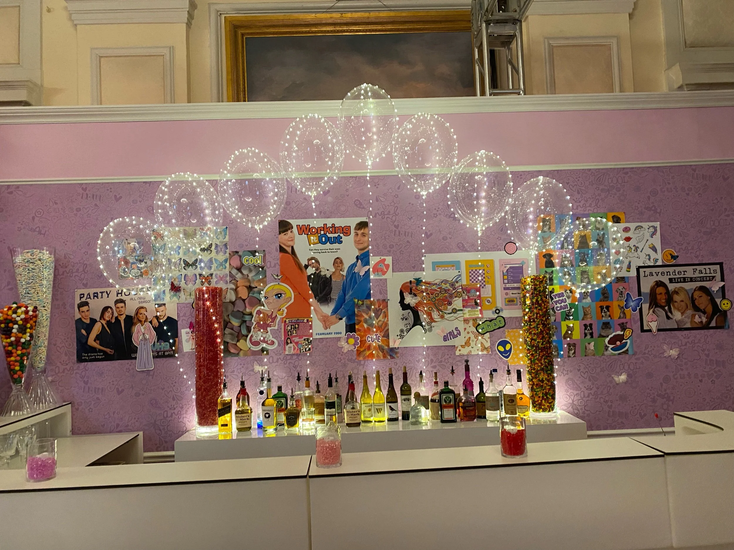 Decorated purple wall with various posters, bottles, colorful candies, and string lights in a festive setting.