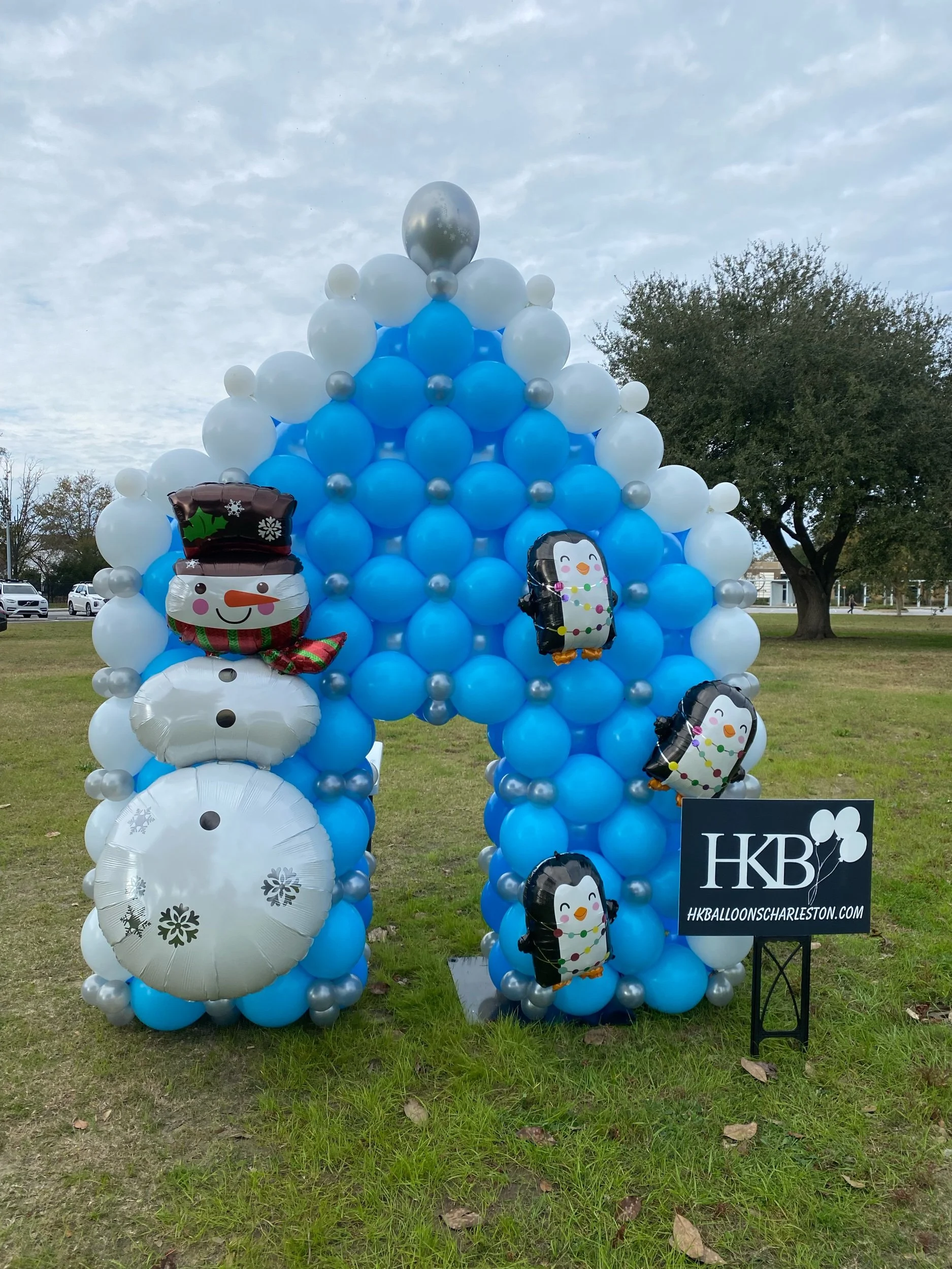 Balloon arrangement with a snowman and penguin Christmas themed balloons, with a sign that reads 'HKB'.