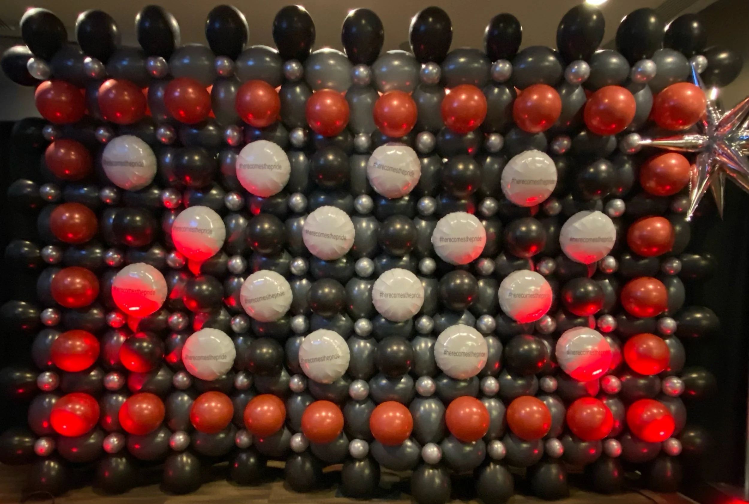 Backdrop decorated with balloons in black, red, silver, and white, adorned with a large silver star-shaped balloon and red lighting effects.