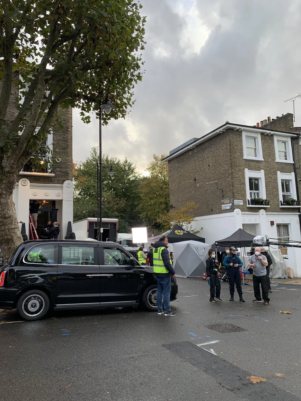 A professional London black cab hero car on a film set with production crew, lighting rigs, and equipment