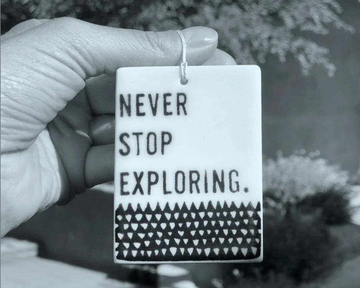 Black and white image with hand holding ceramic art that reads: NEVER STOP EXPLORING