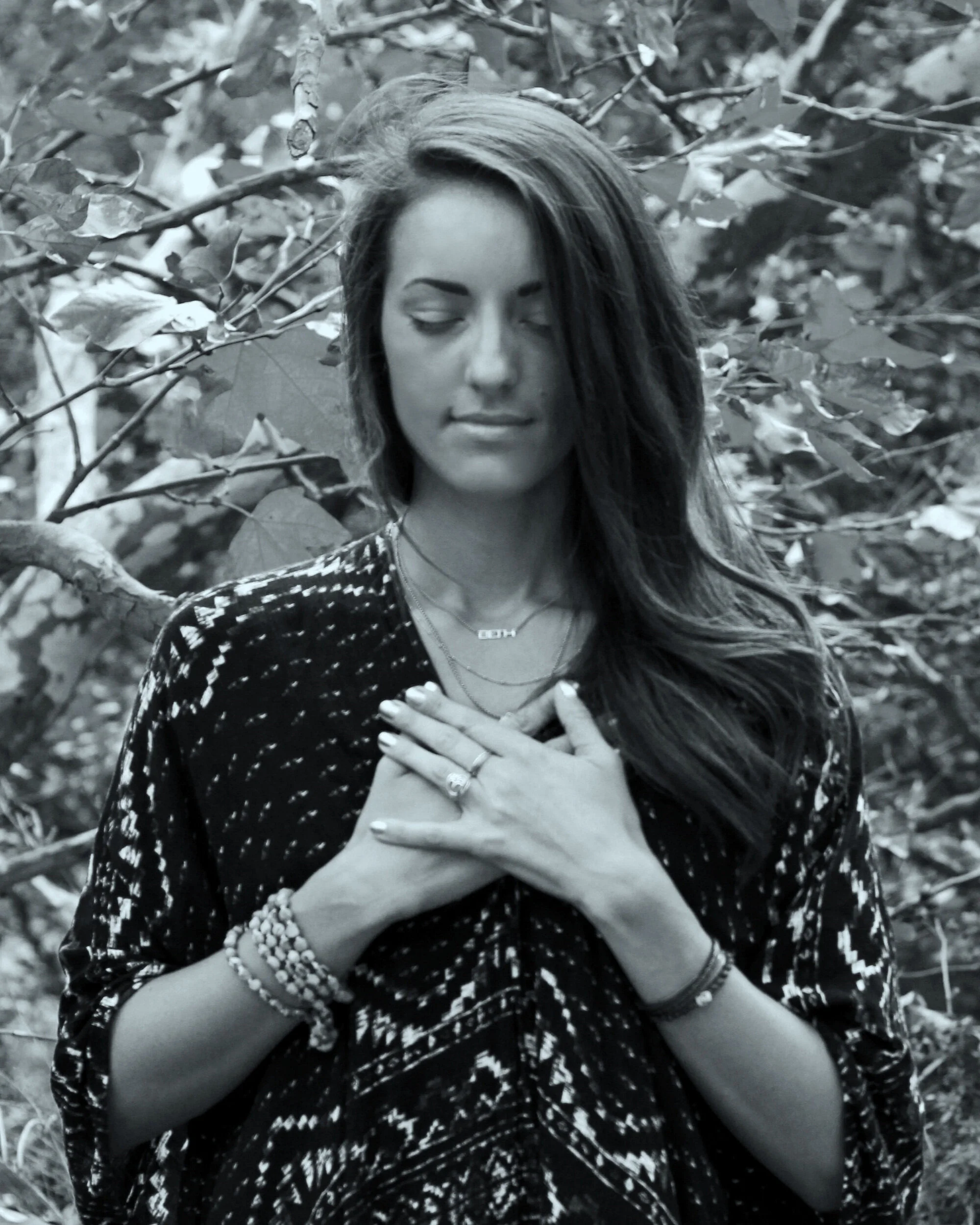 Beth standing in the trees with eyes closed, facing camera with hands over her heart.