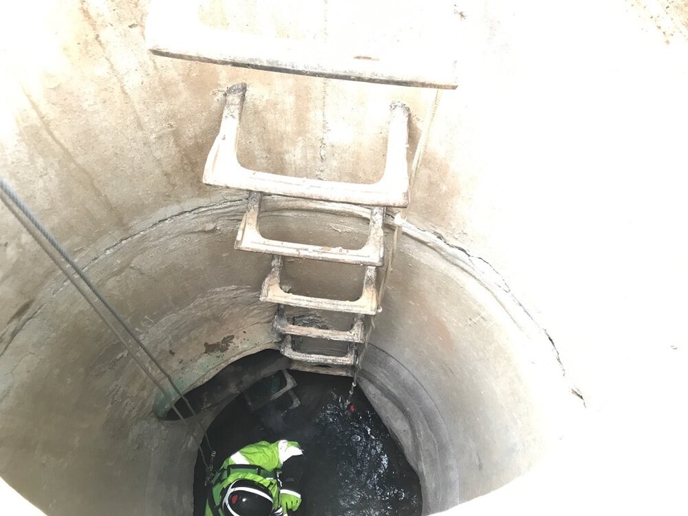  A worker inspects a manhole, taking photos and measurements.  