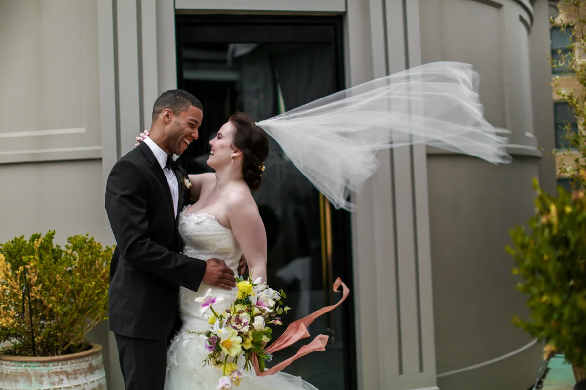 NoMad Hotel Rooftop Wedding in New York City - The bride and groom pose for windswept rooftop wedding portraits and the bride’s Jaclyn Jordan wedding veil blows in the wind.