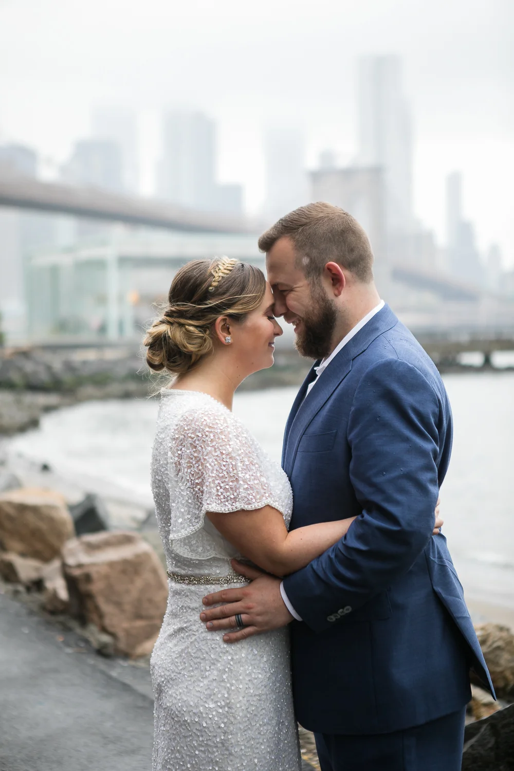 Wedding photos in front of the Brooklyn Bridge. New York Bride in a short wedding dress and groom in a blue suit pose in front of the Brooklyn Bridge. | Intimate Wedding at the Malthouse in Manhattan, New York City.