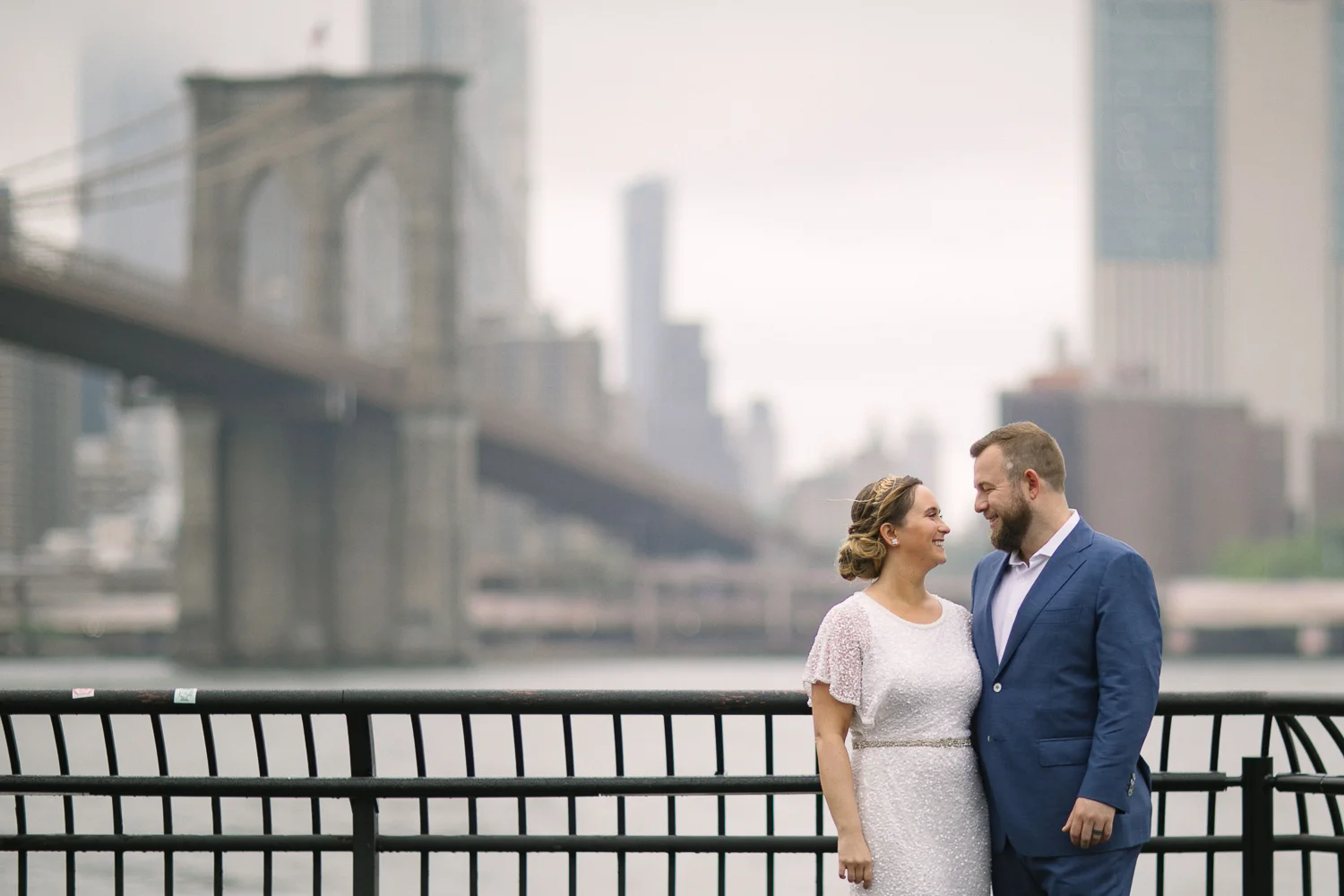 Brooklyn Bridge wedding portraits. New York Bride in a short wedding dress and groom in a blue suit pose in front of the Brooklyn Bridge. | Intimate Wedding at the Malthouse in Manhattan, New York City.
