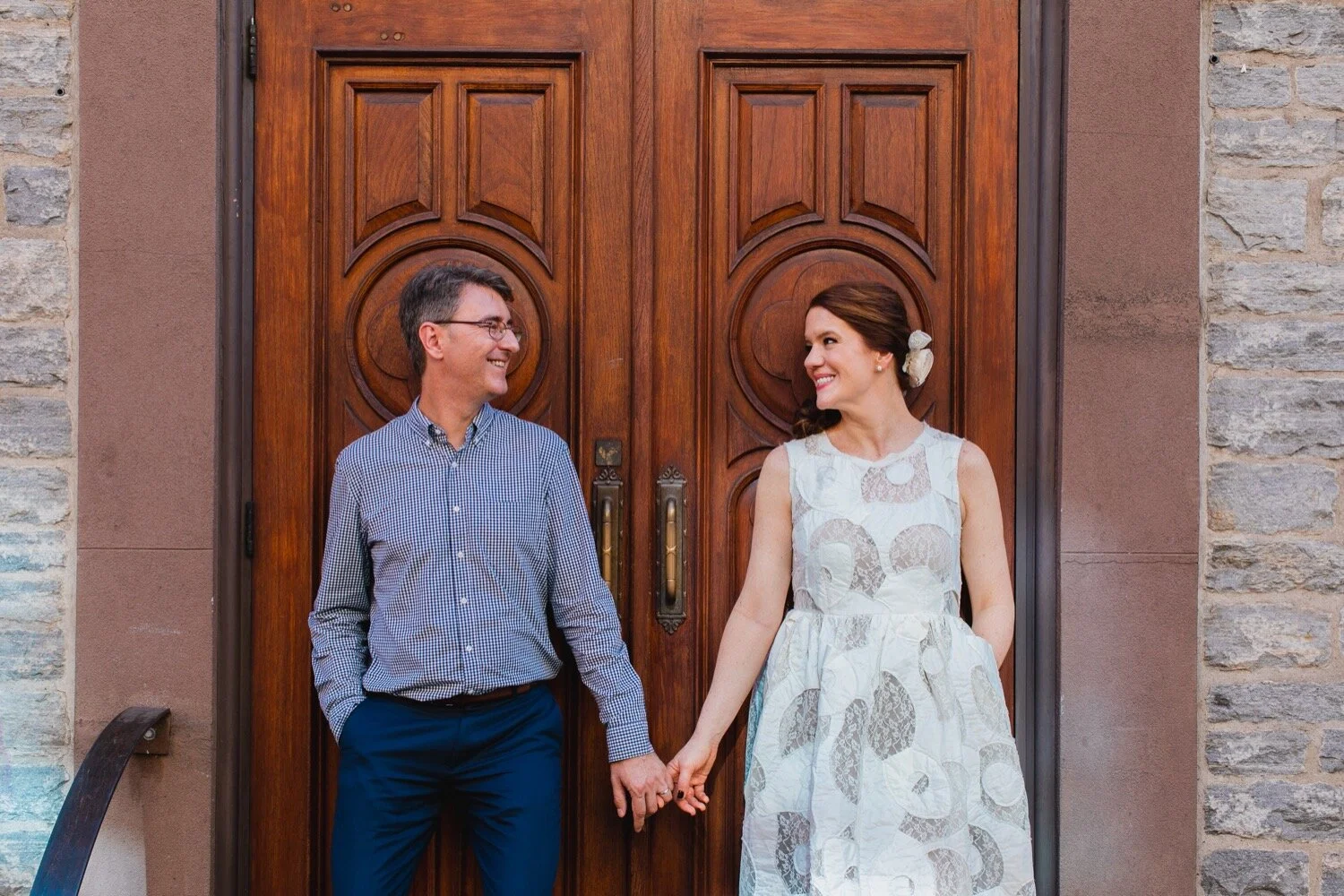 Bride and groom holding hands and smiling in front of a door of a church.
