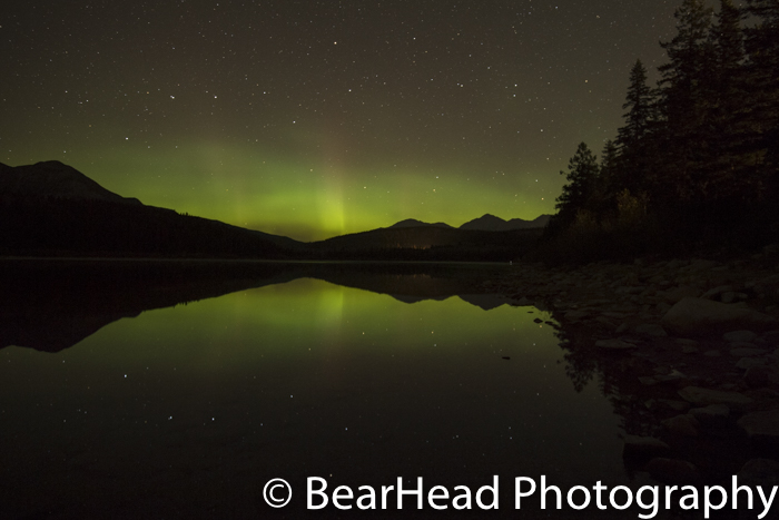The northern lights and the big dipper are reflected into the lake.