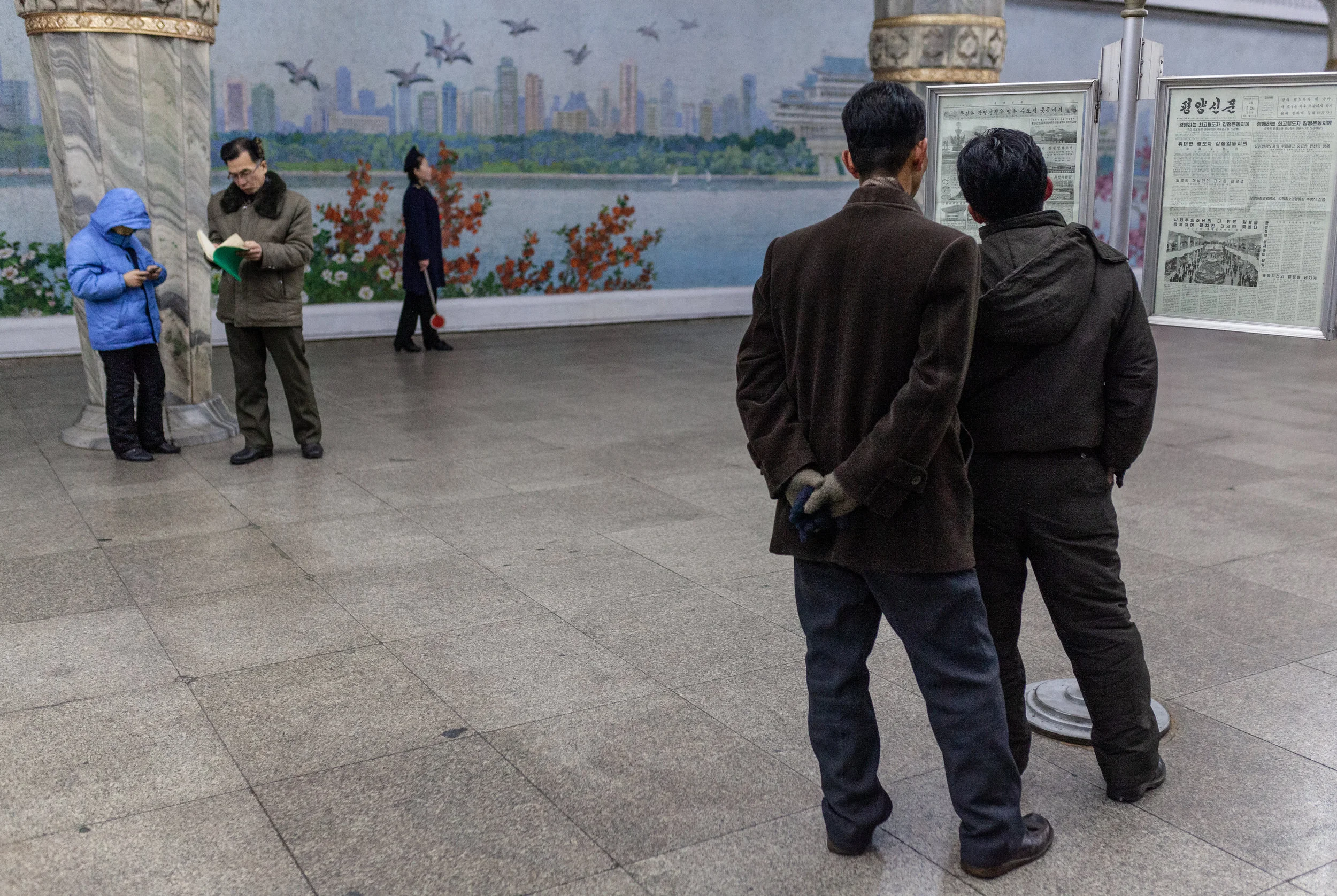 Two men catch up on the daily news from the imaginatively titled "Pyongyang Newspaper" while waiting for the metro.
