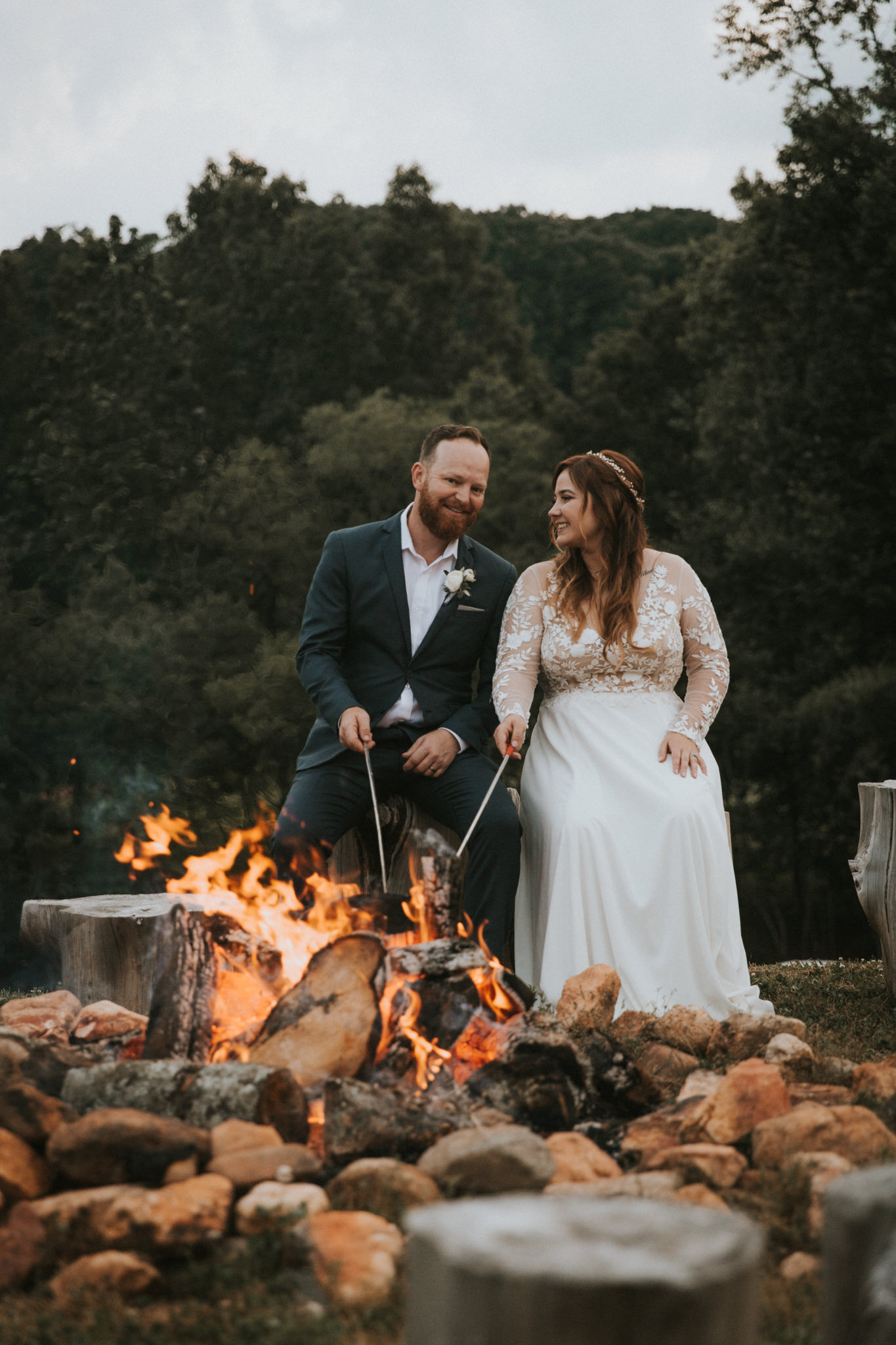 A couple roasts marshmallows by the campfire on their intimate wedding day