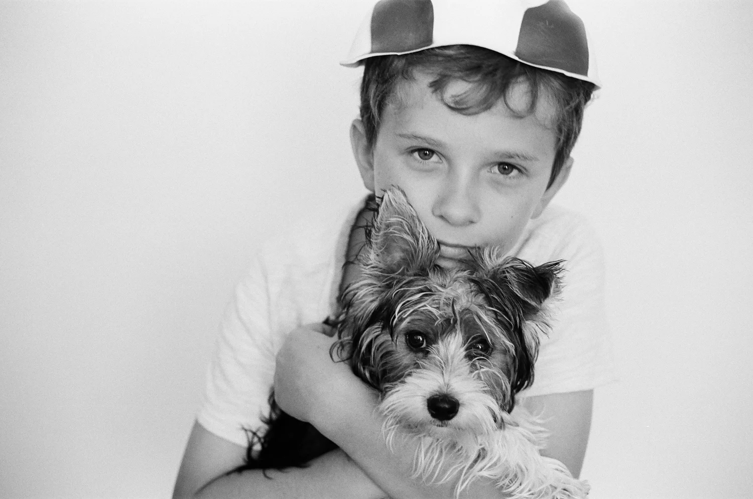 A boy hugging his yorkie dog and looking into the film camera.